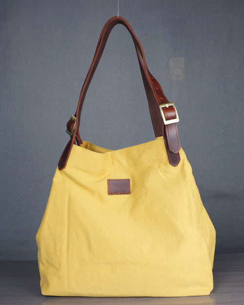 Yellow handbag with brown leather handle and strap on a gray background