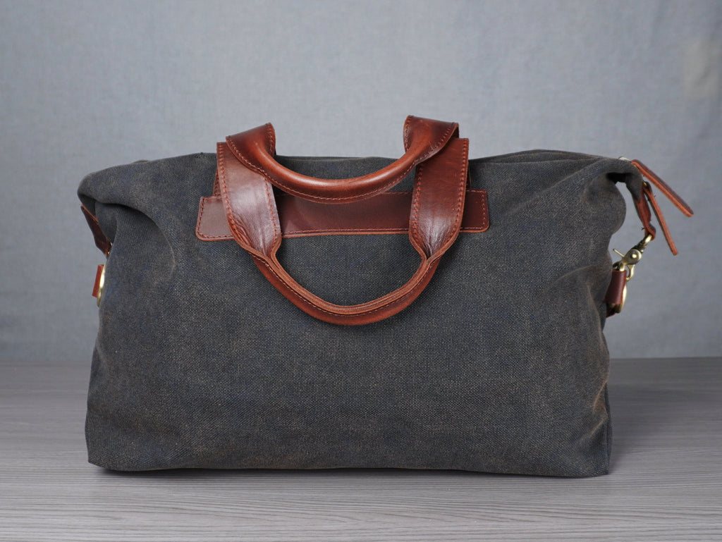 Gray bag with brown leather handles on a grey surface against a plain background
