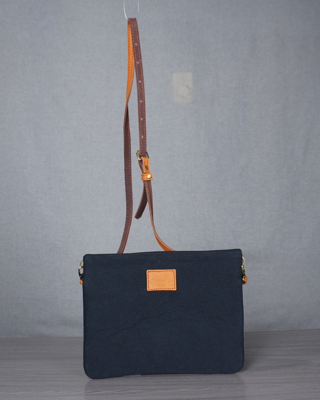 Black handbag with a brown leather strap on a gray background