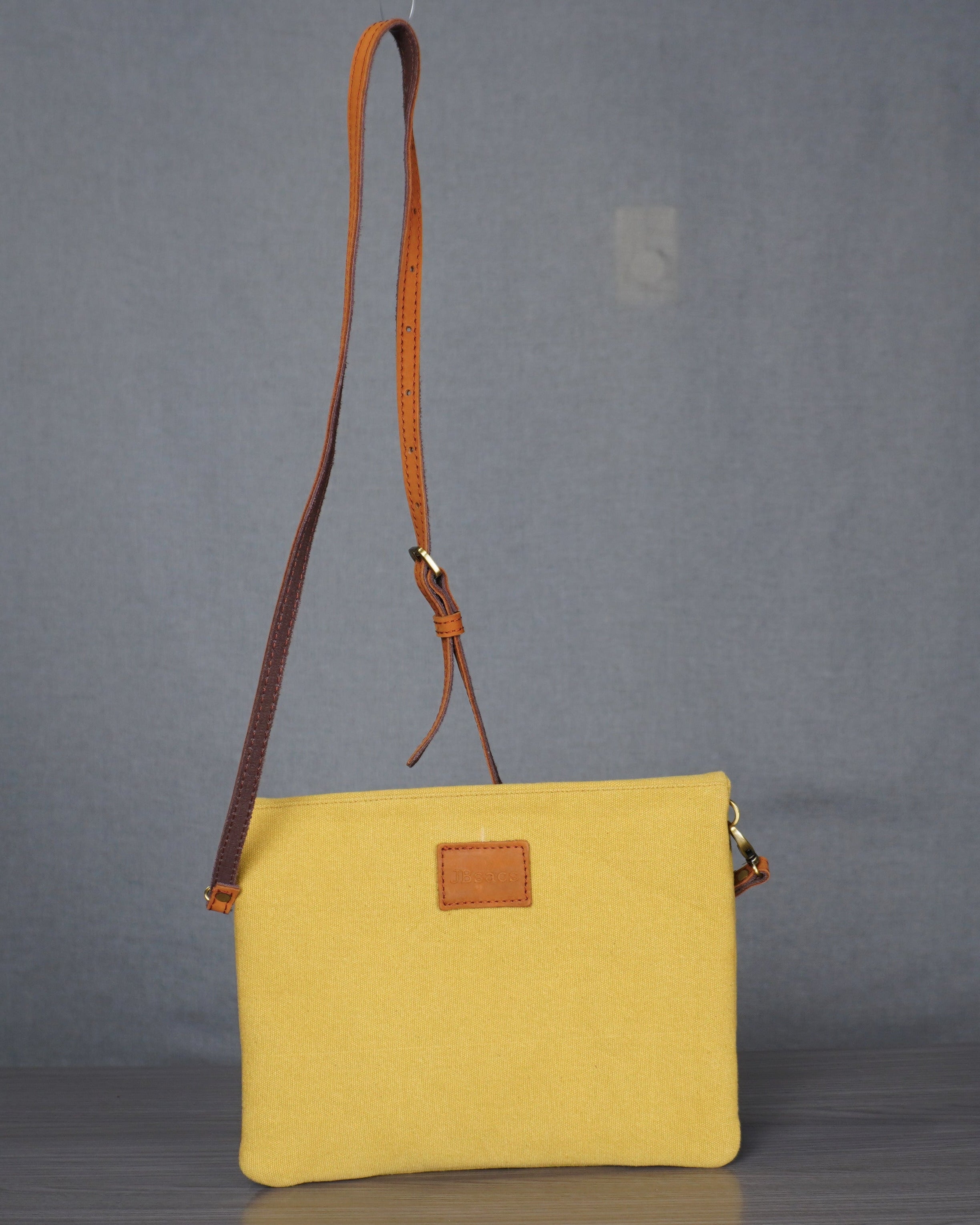Yellow crossbody bag with brown strap on a gray floor against a plain backdrop