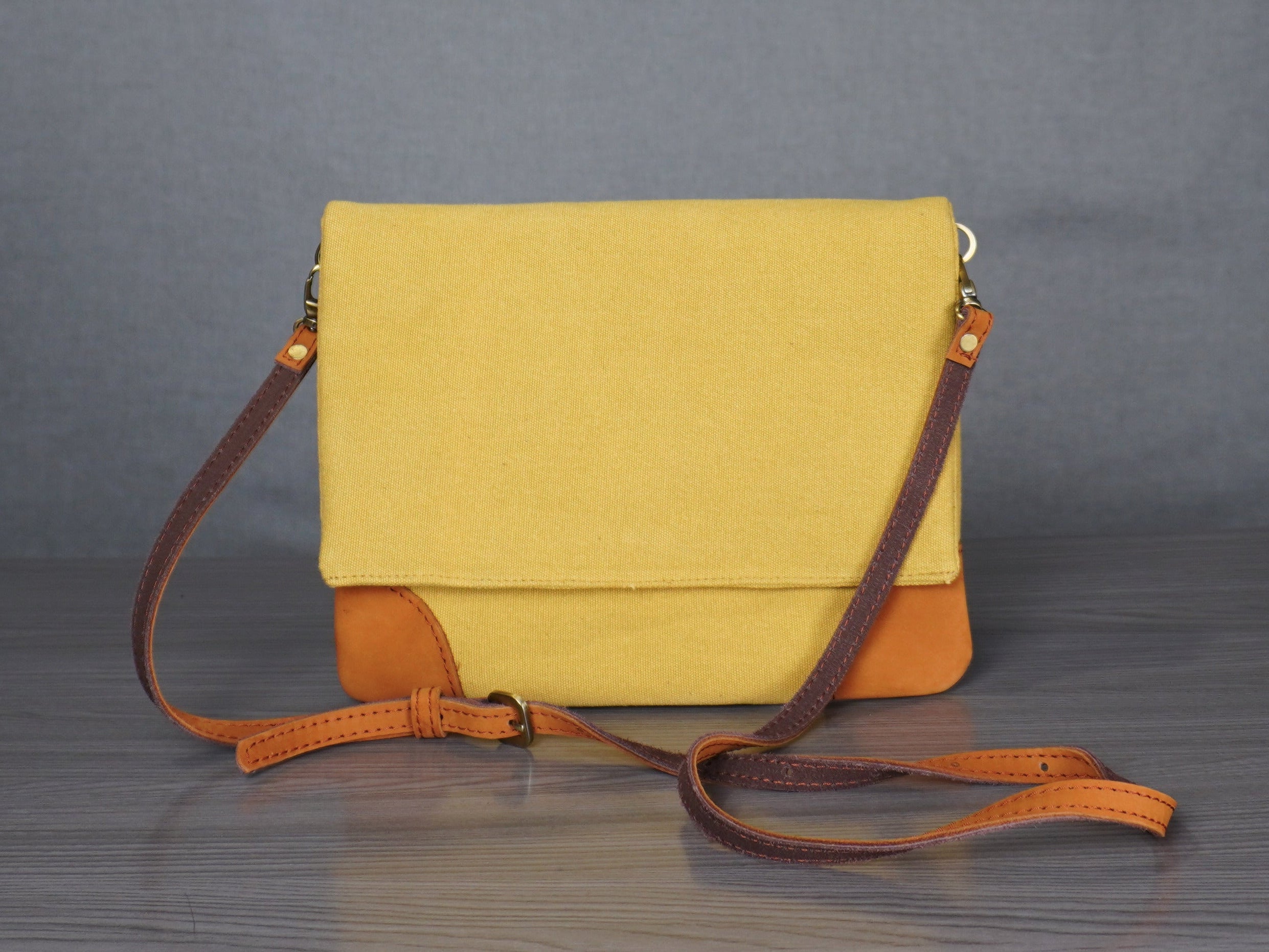 Yellow handbag with brown strap on a gray floor against a plain backdrop