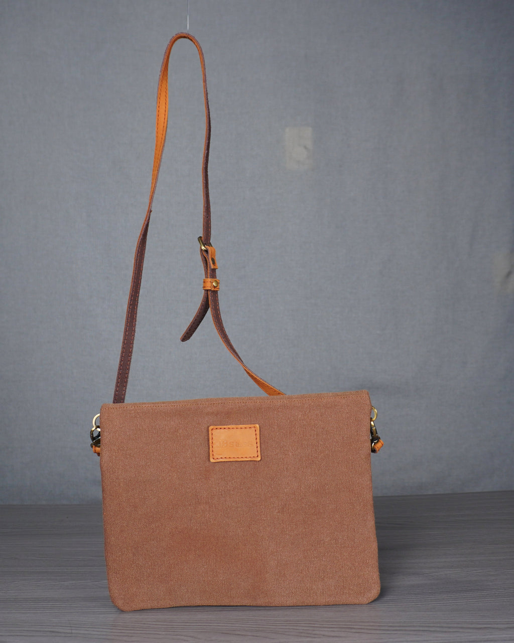 Brown handbag with a leather strap on a gray floor against a plain backdrop