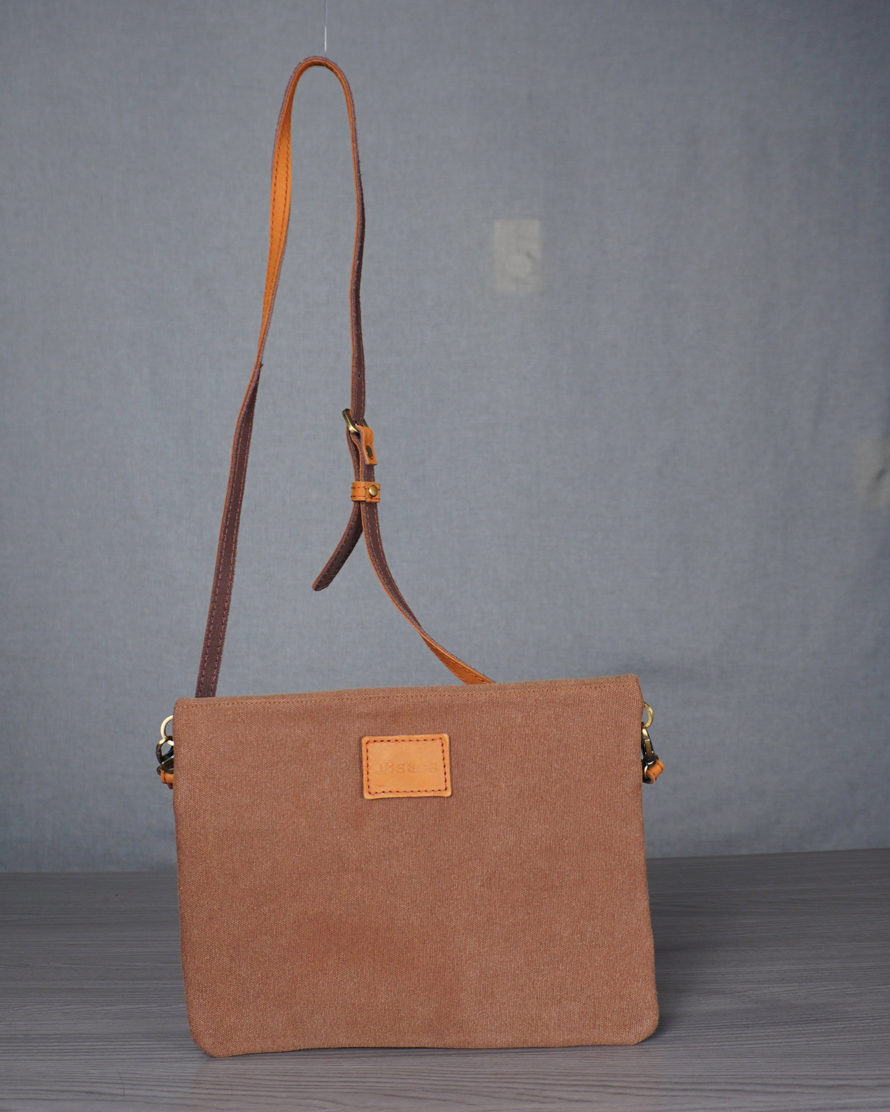Brown handbag with a leather strap on a gray floor against a plain backdrop
