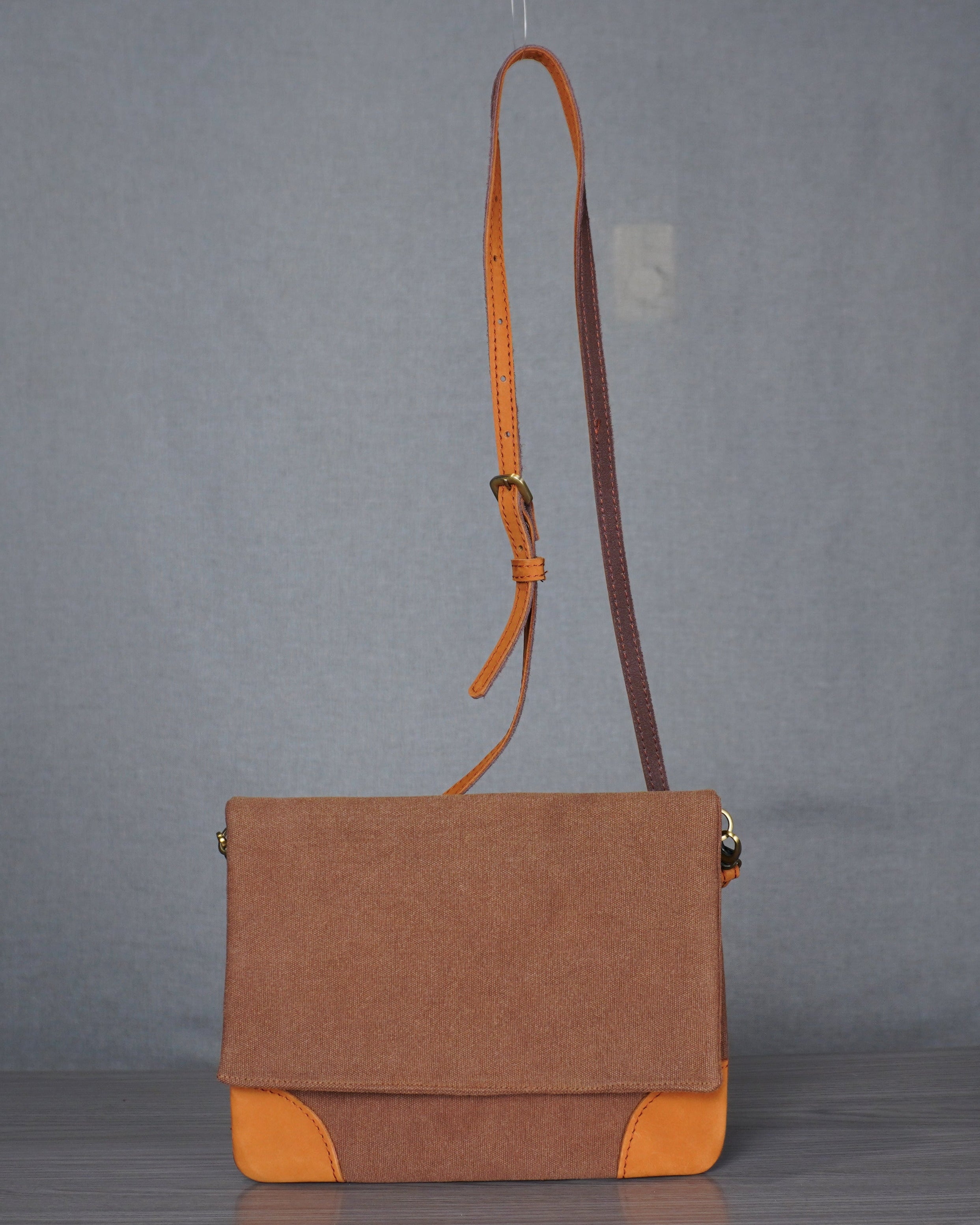 Brown bag with orange leather accents on a gray floor against a gray backdrop