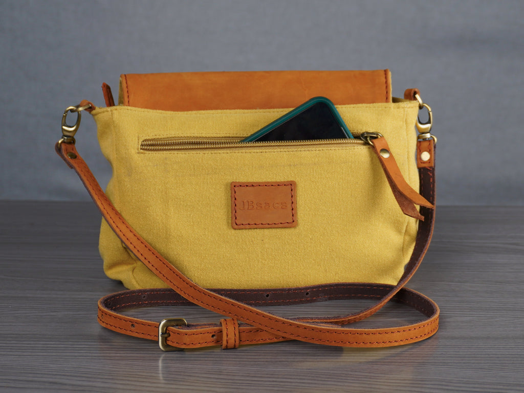 Yellow handbag with brown strap on a gray surface