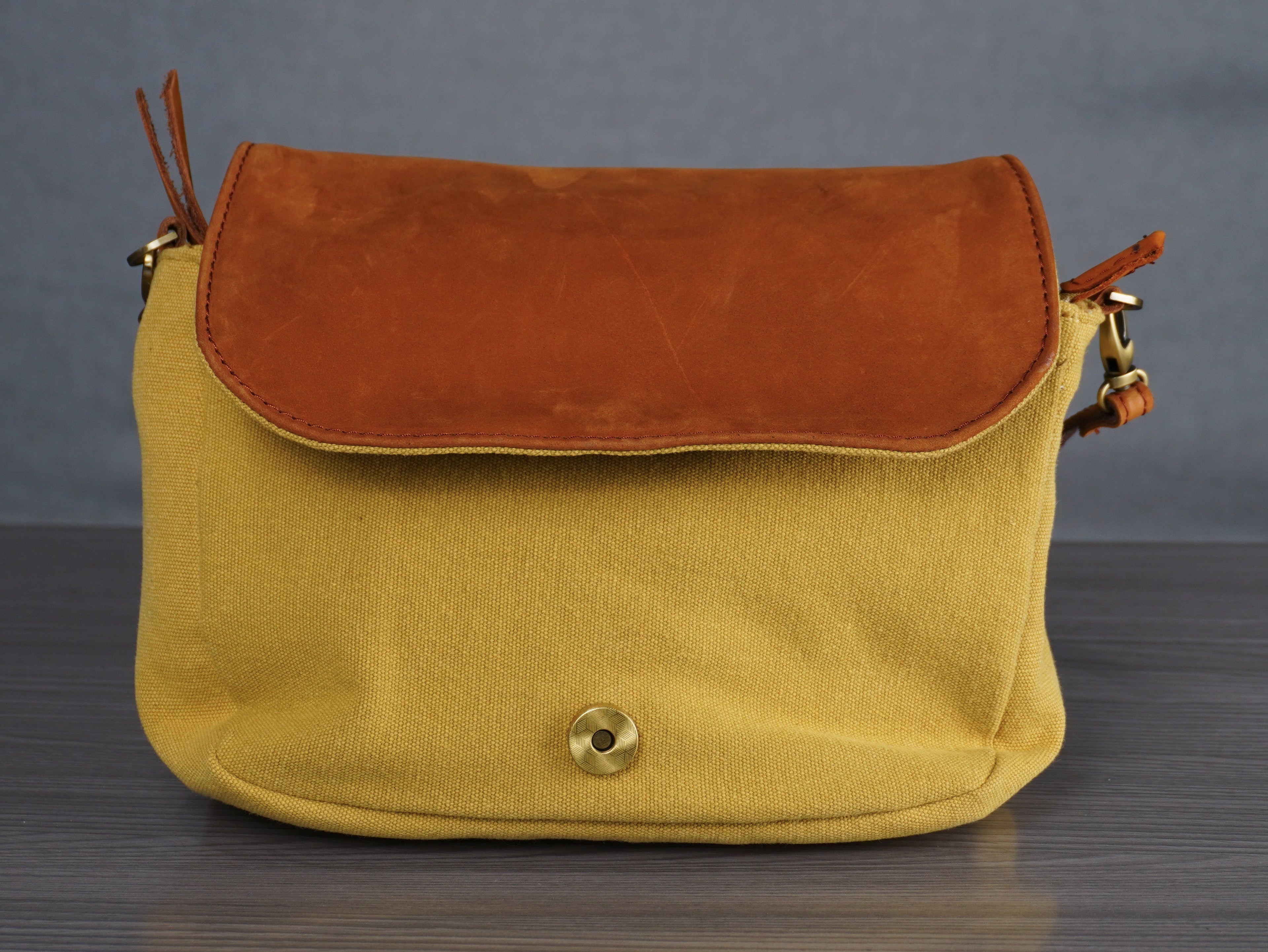 Yellow handbag with brown flap on a gray surface and background