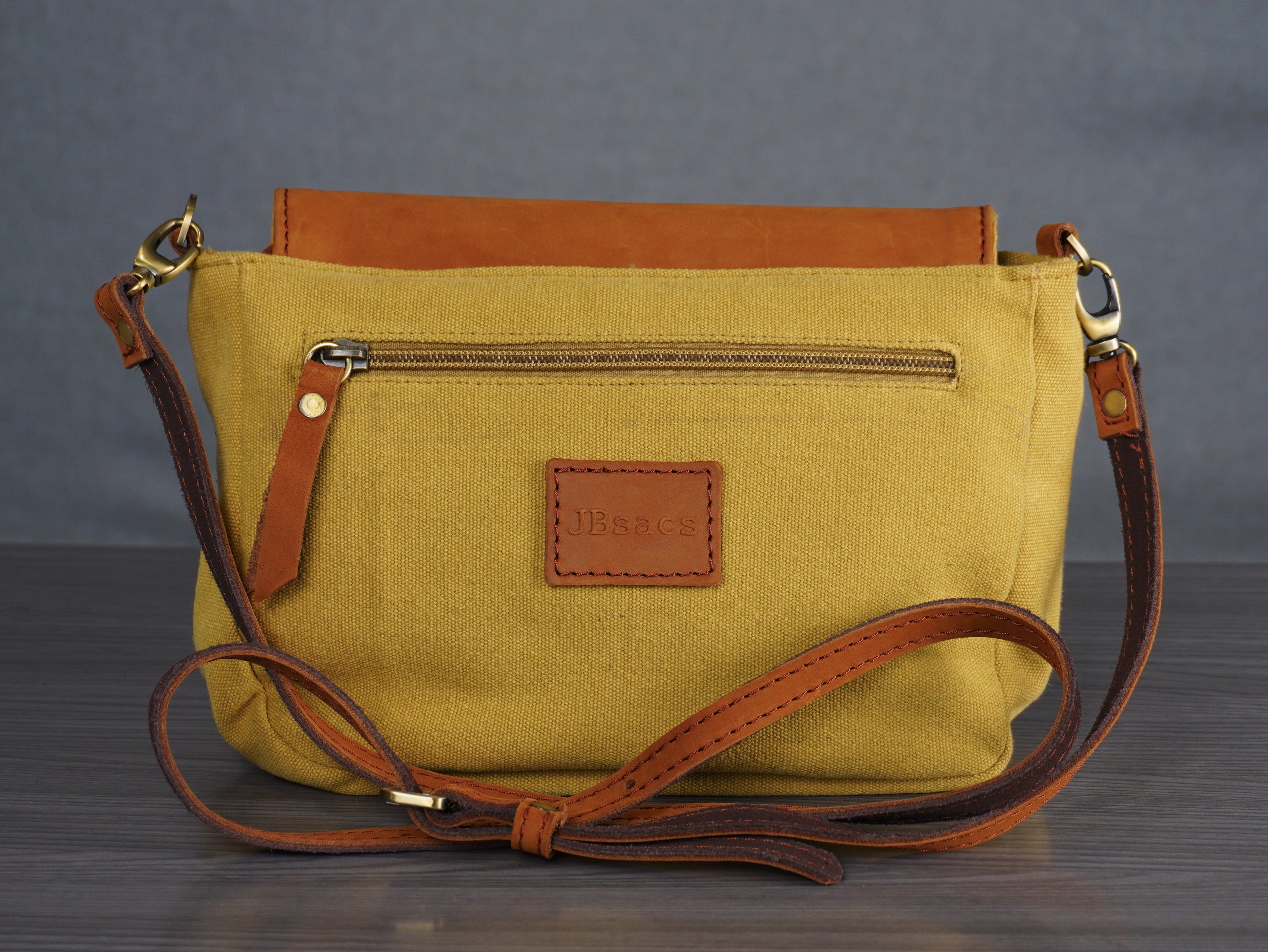 Yellow handbag with brown leather accents on a gray background