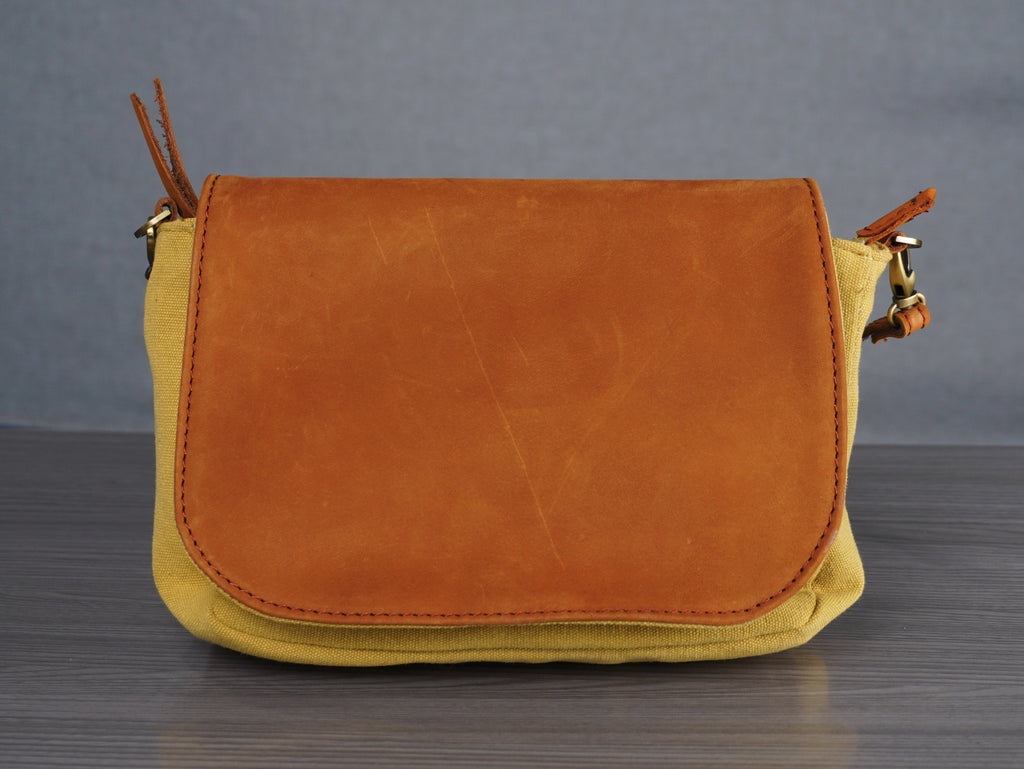 Brown leather and yellow canvas crossbody bag on a gray surface with a gray background