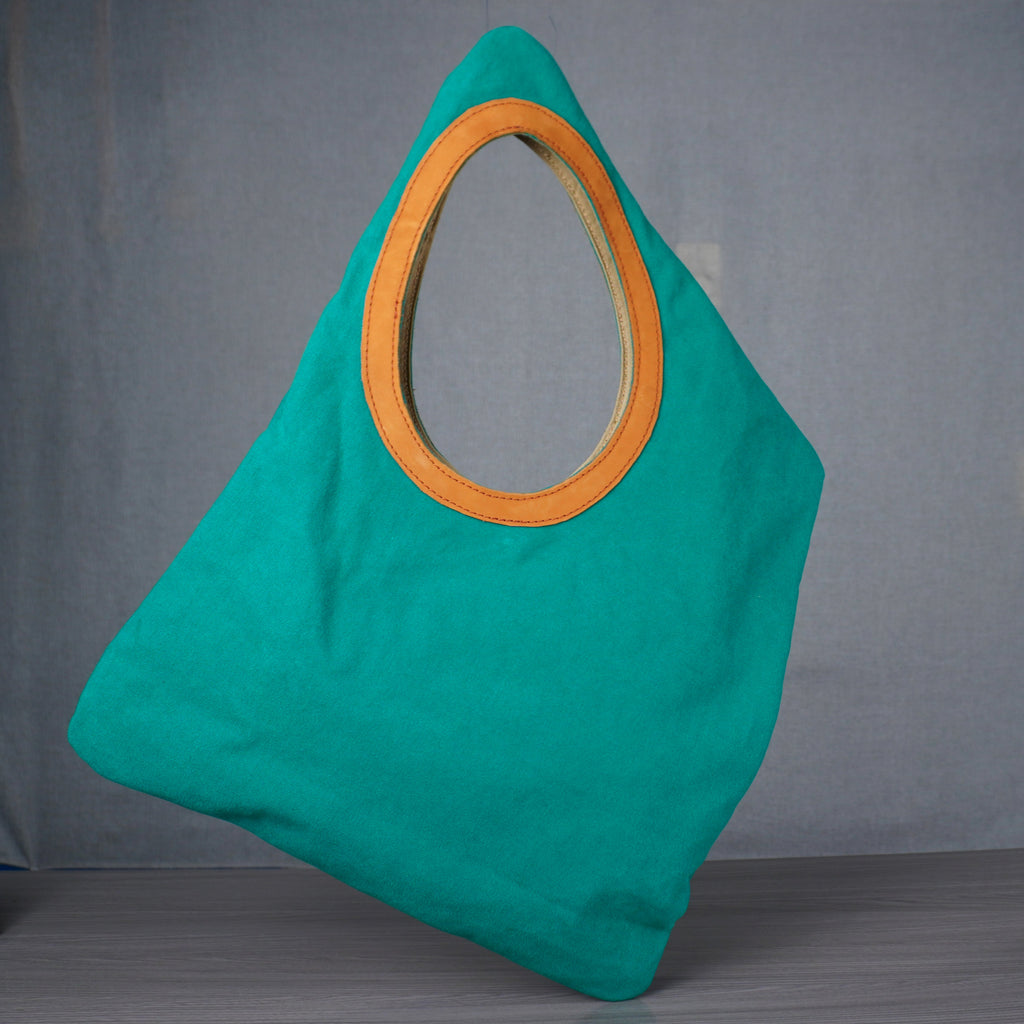 Turquoise bag with orange handle on a gray floor against a gray wall.
