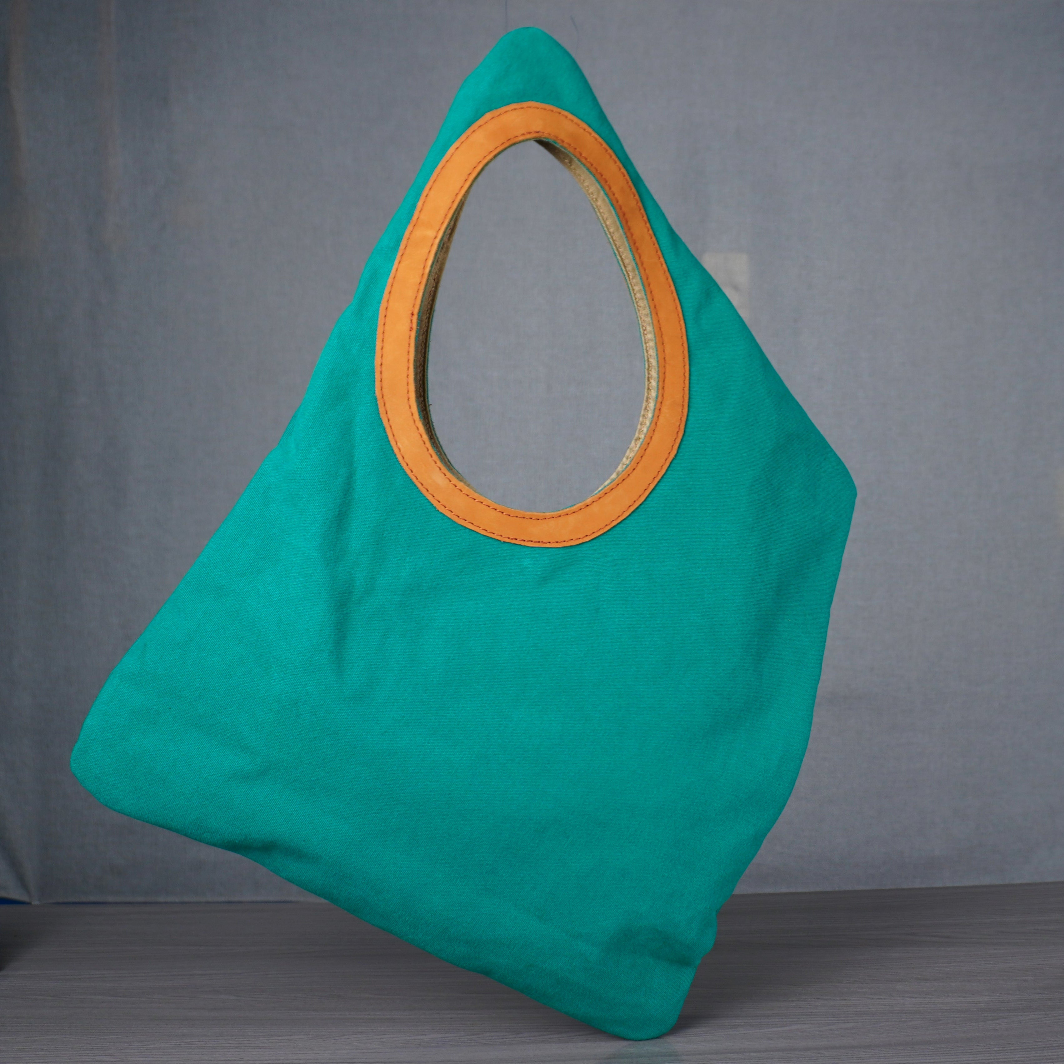 Turquoise bag with orange handle on a gray floor against a gray wall.