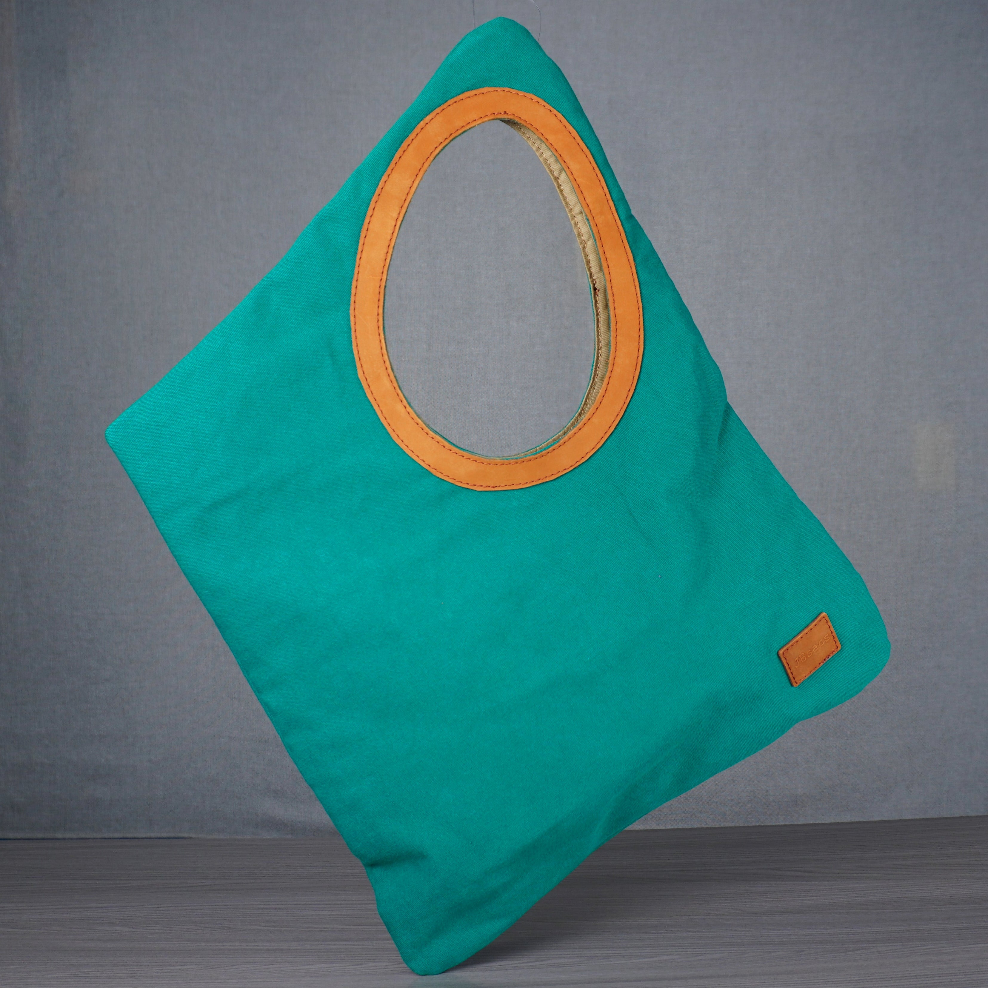 Teal bag with a yellow circular detail on a gray floor against a gray wall.