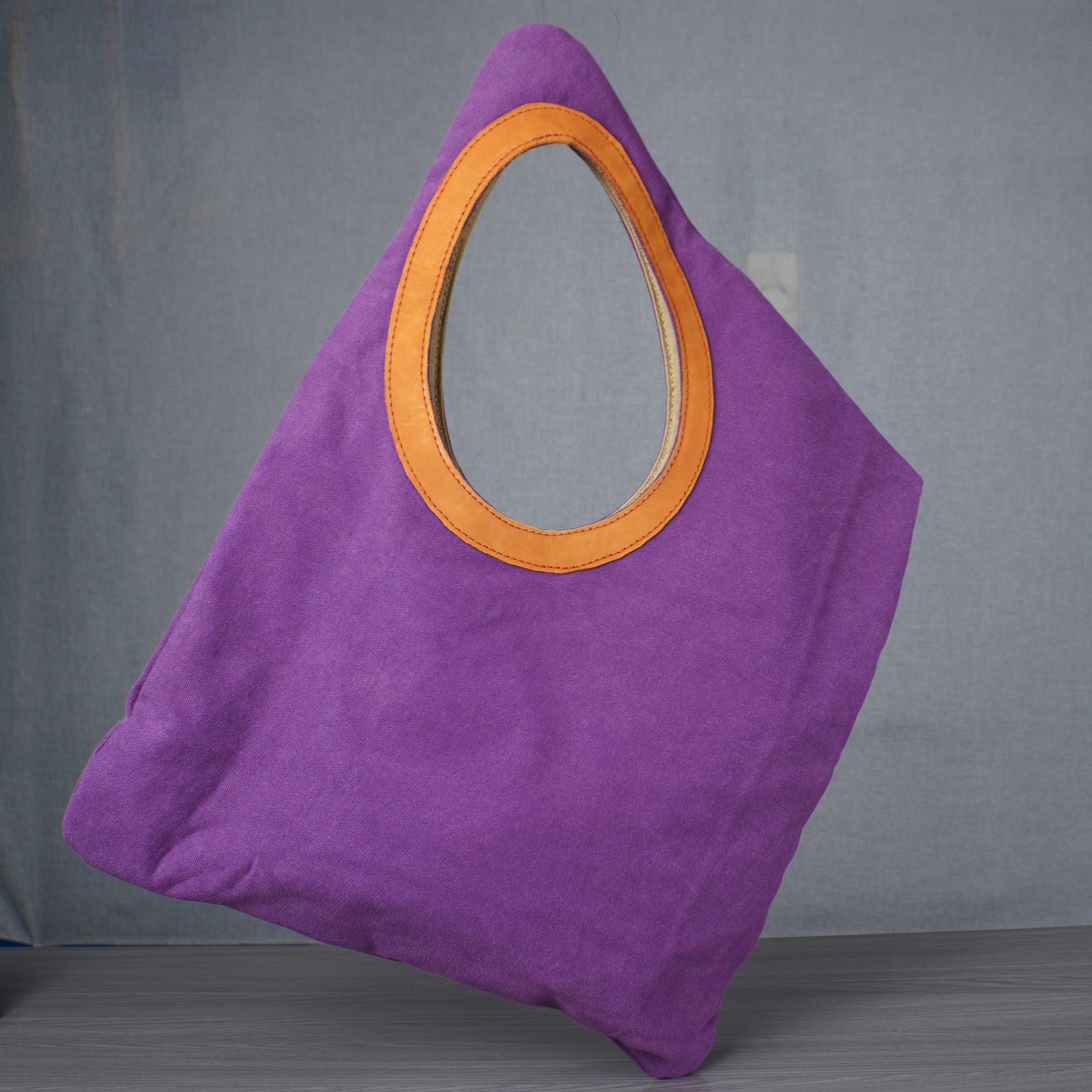 Purple bag with a yellow circular detail on a gray floor against a gray wall.