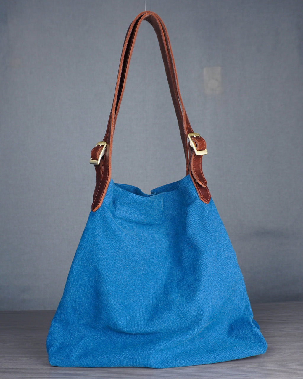 Blue handbag with brown leather handle on a gray background