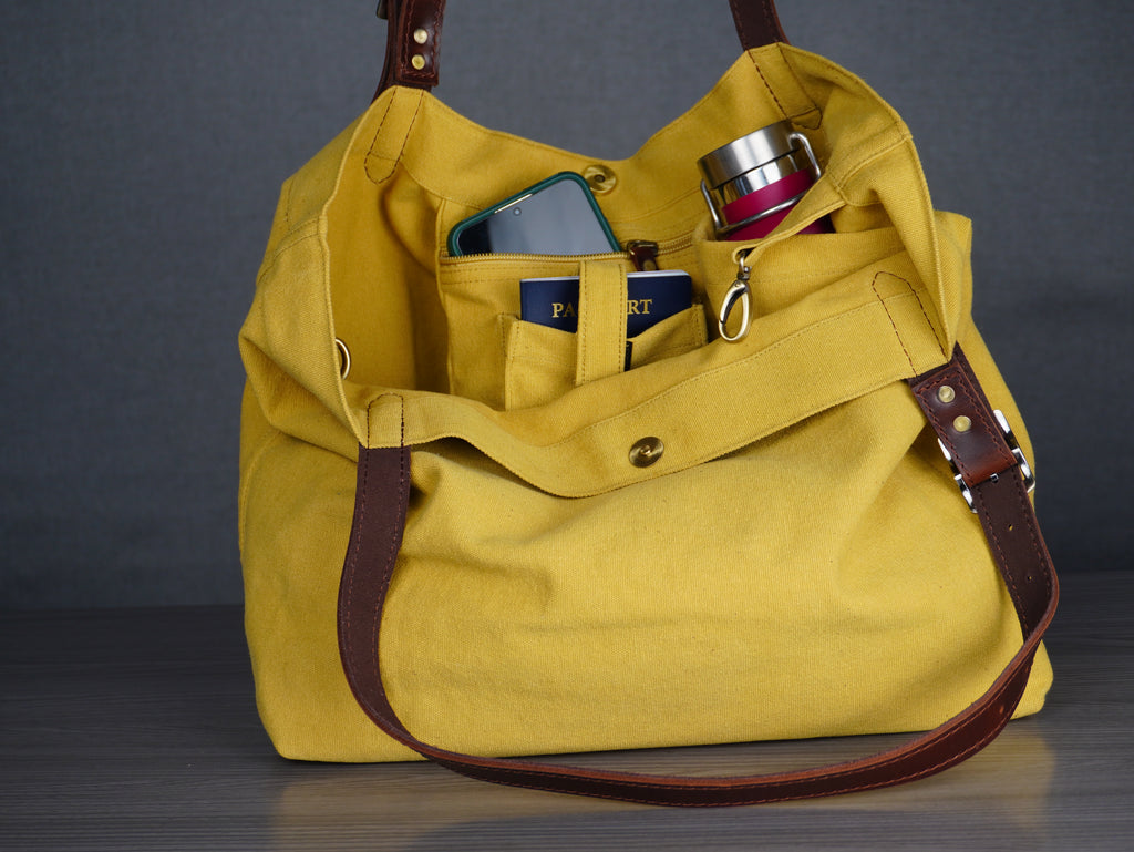 Yellow handbag with brown straps containing a phone, wallet, and mug on a dark background