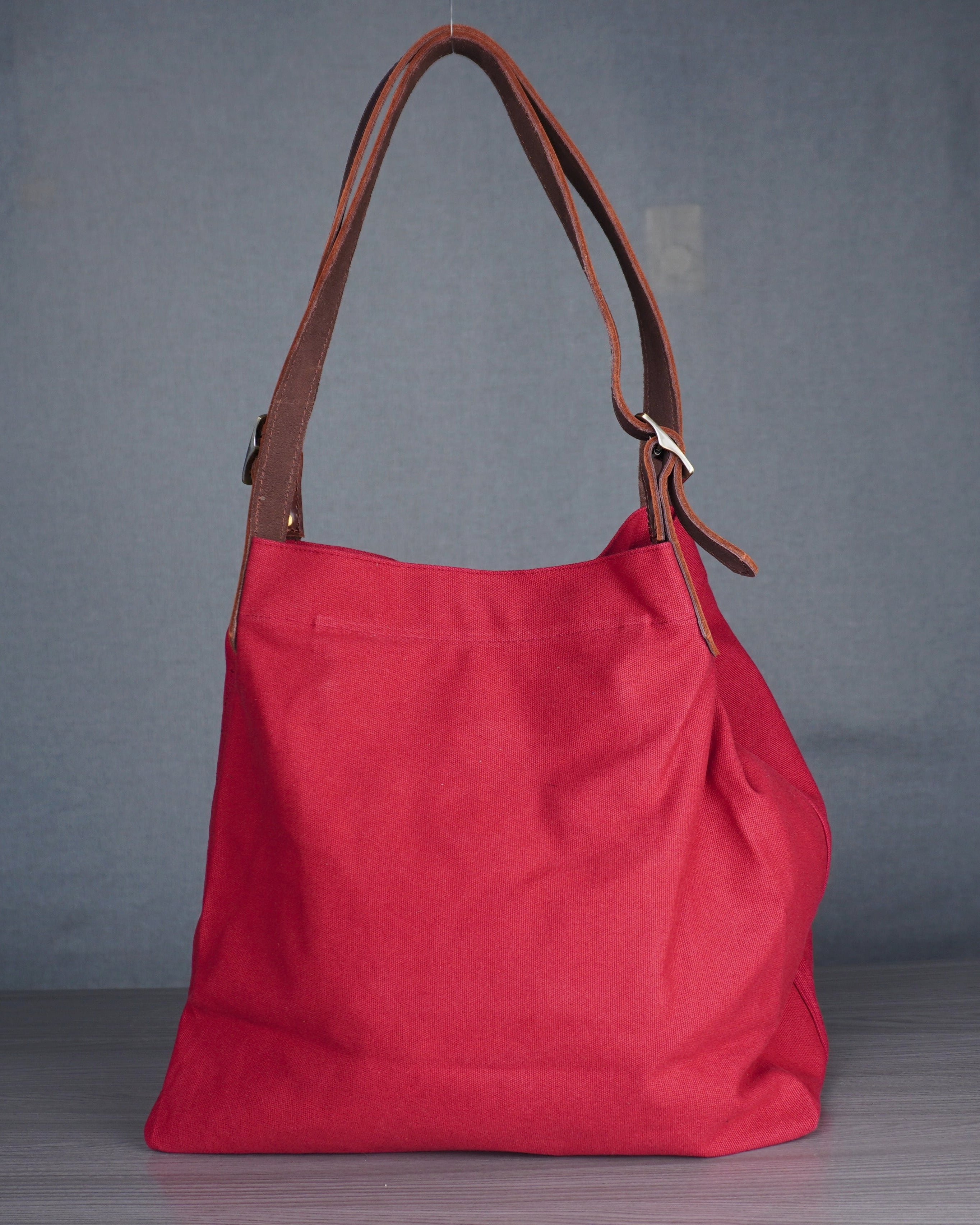 Red handbag with brown leather handle on a gray background