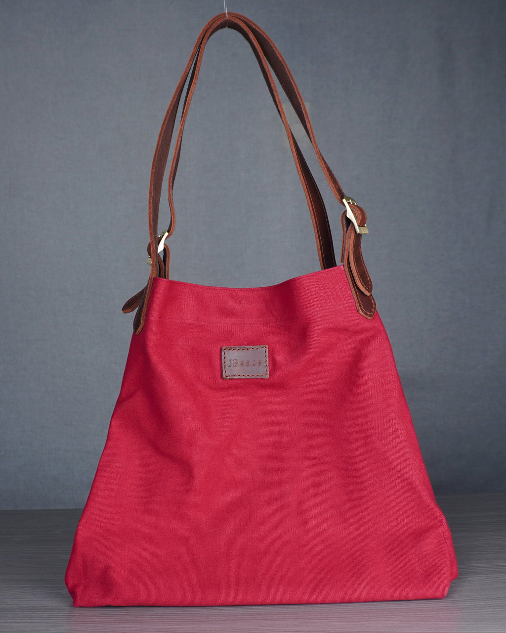Red handbag with brown leather handles on a gray floor against a blue wall.