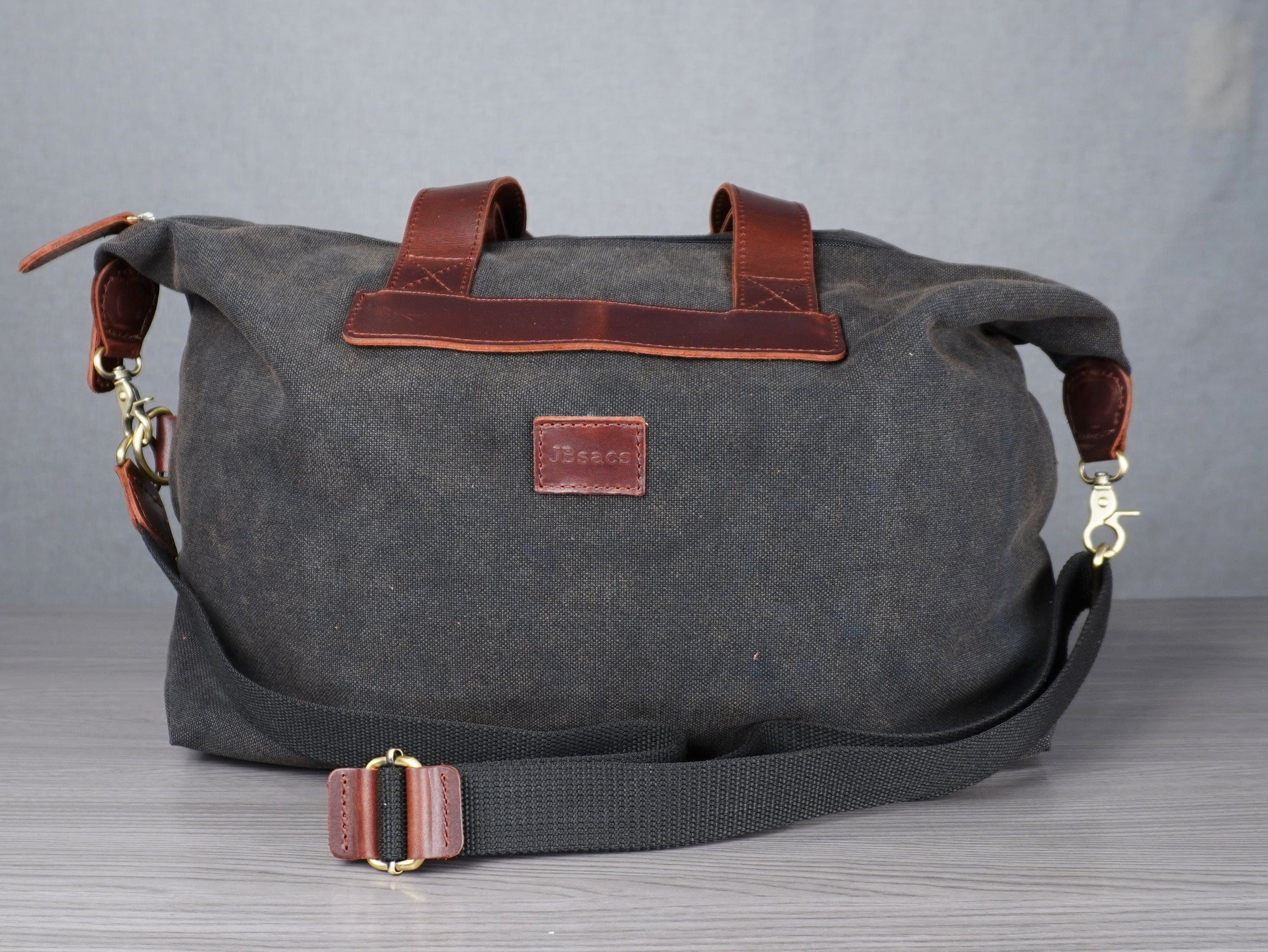 Gray bag with brown leather accents on a metal table against a plain background 