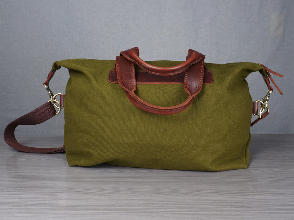Green bag with brown handles and strap on a grey surface