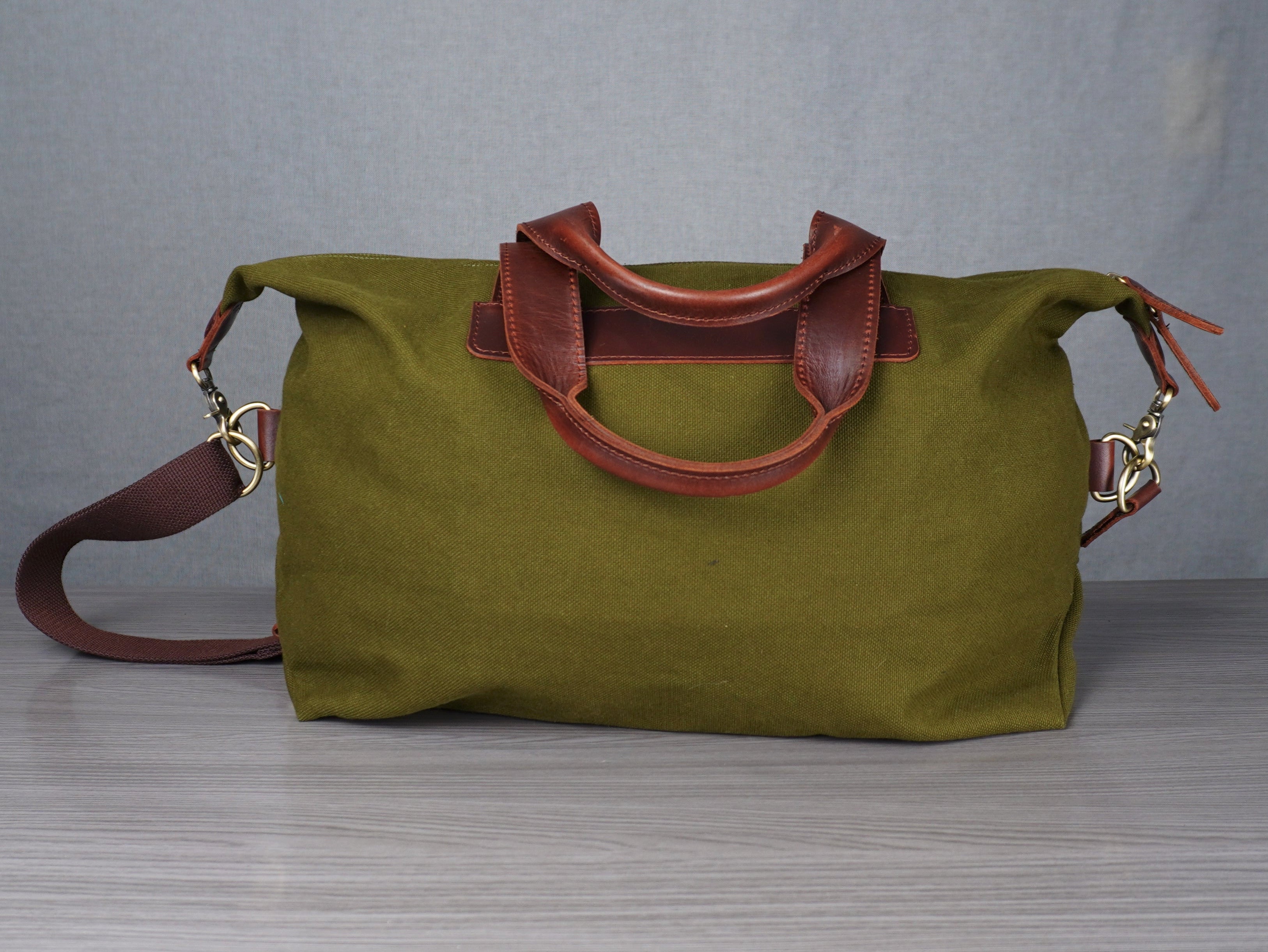 Green bag with brown handles and strap on a grey surface