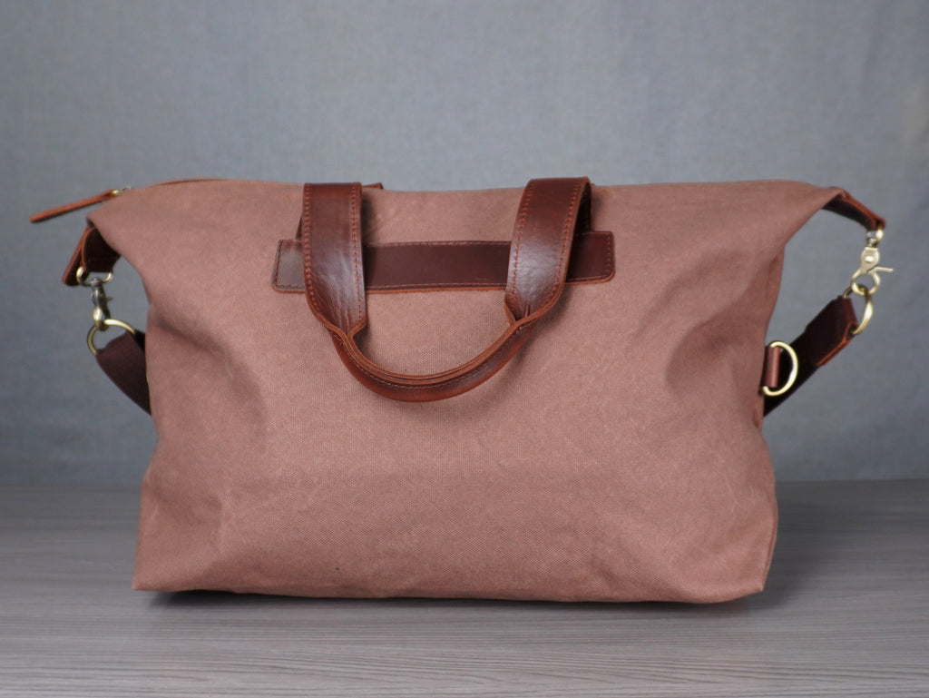 tan handbag with brown leather handles on a metal surface against a plain background