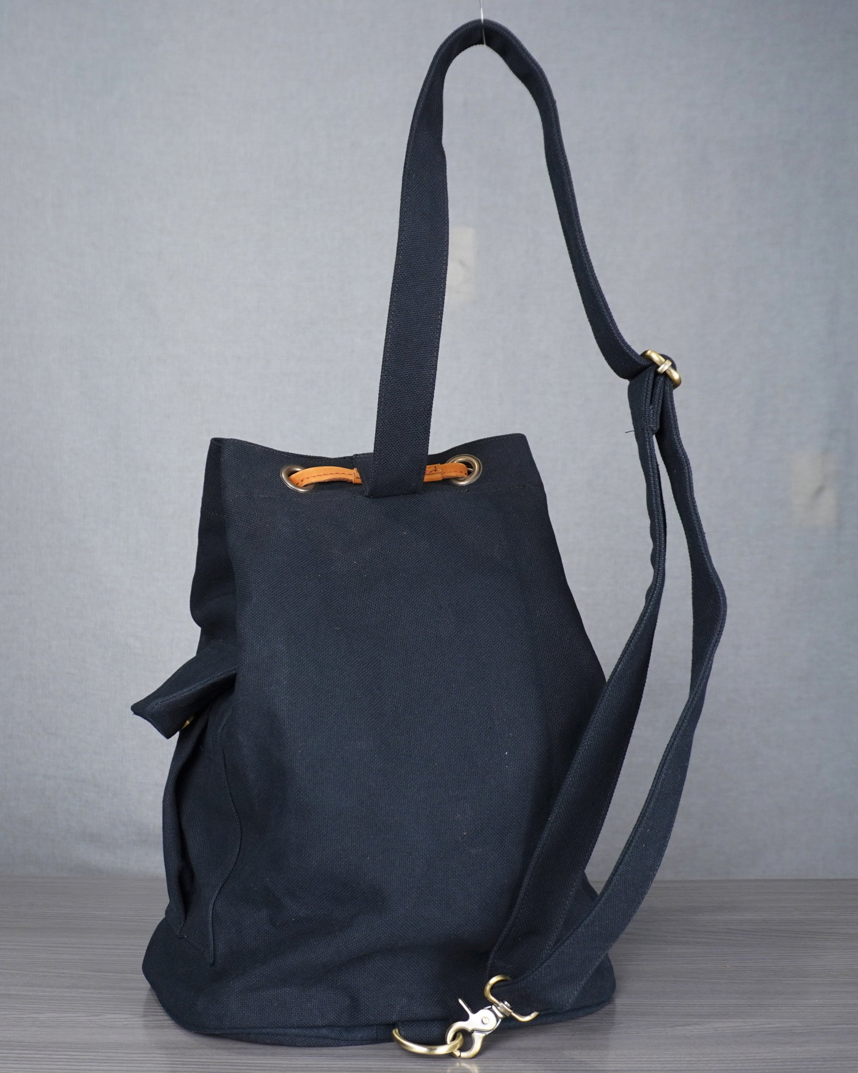 Black backpack with a strap on a gray surface against a blue and white background