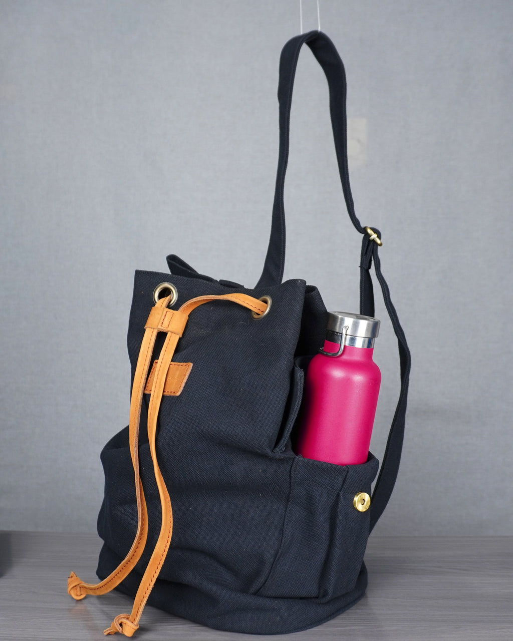 Black backpack with orange drawstrings and a pink water bottle on a gray floor.