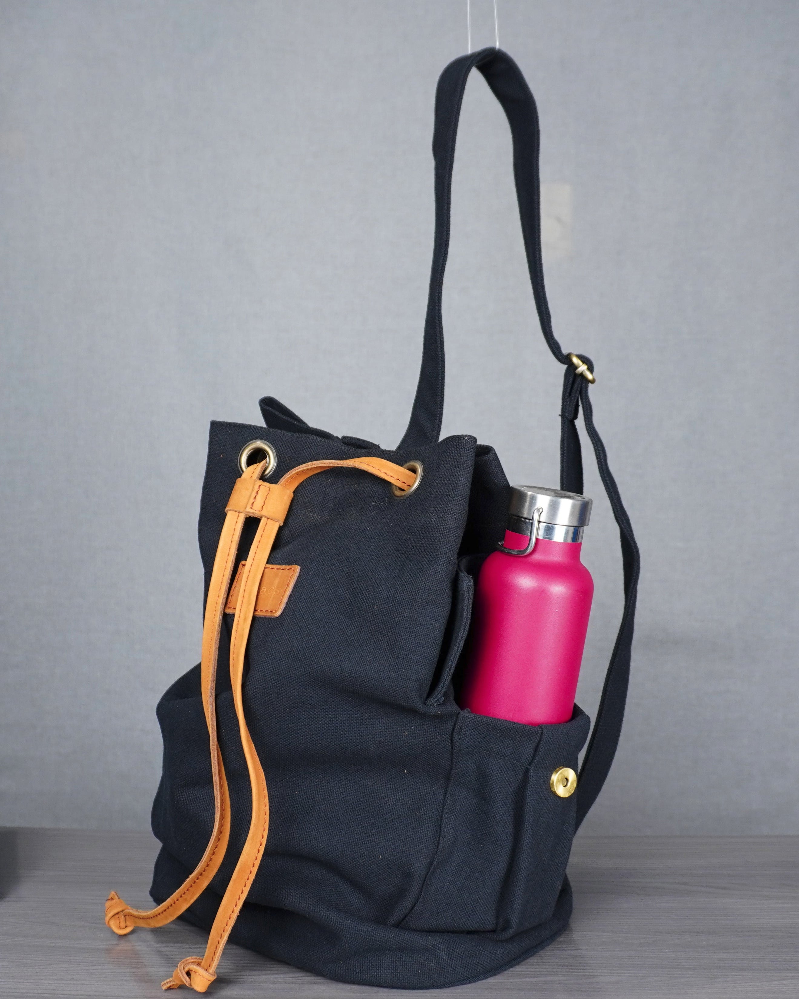 Black backpack with orange drawstrings and a pink water bottle on a gray floor.