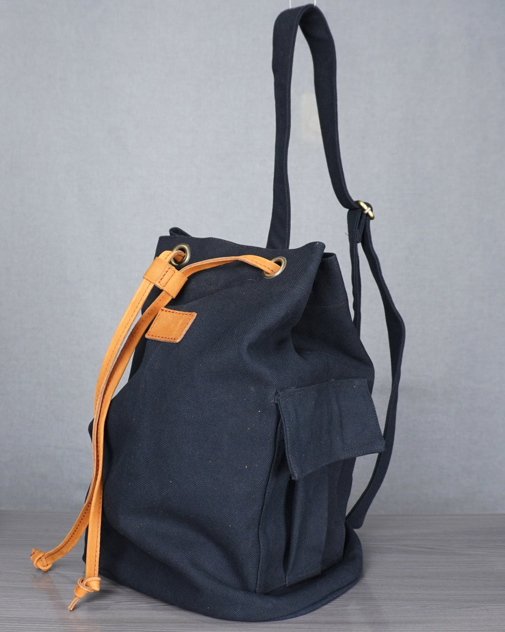 Black backpack with orange drawstring on a gray floor against a gray backdrop