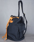 Black backpack with orange drawstring on a gray floor against a gray backdrop