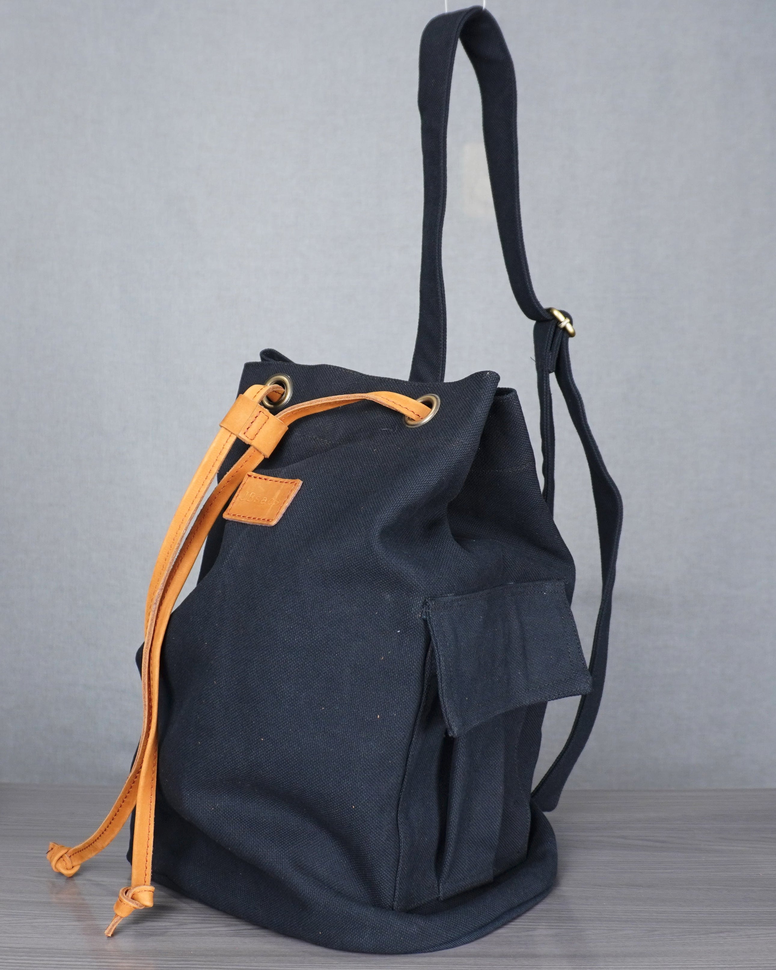 Black backpack with orange drawstring on a gray floor against a gray backdrop