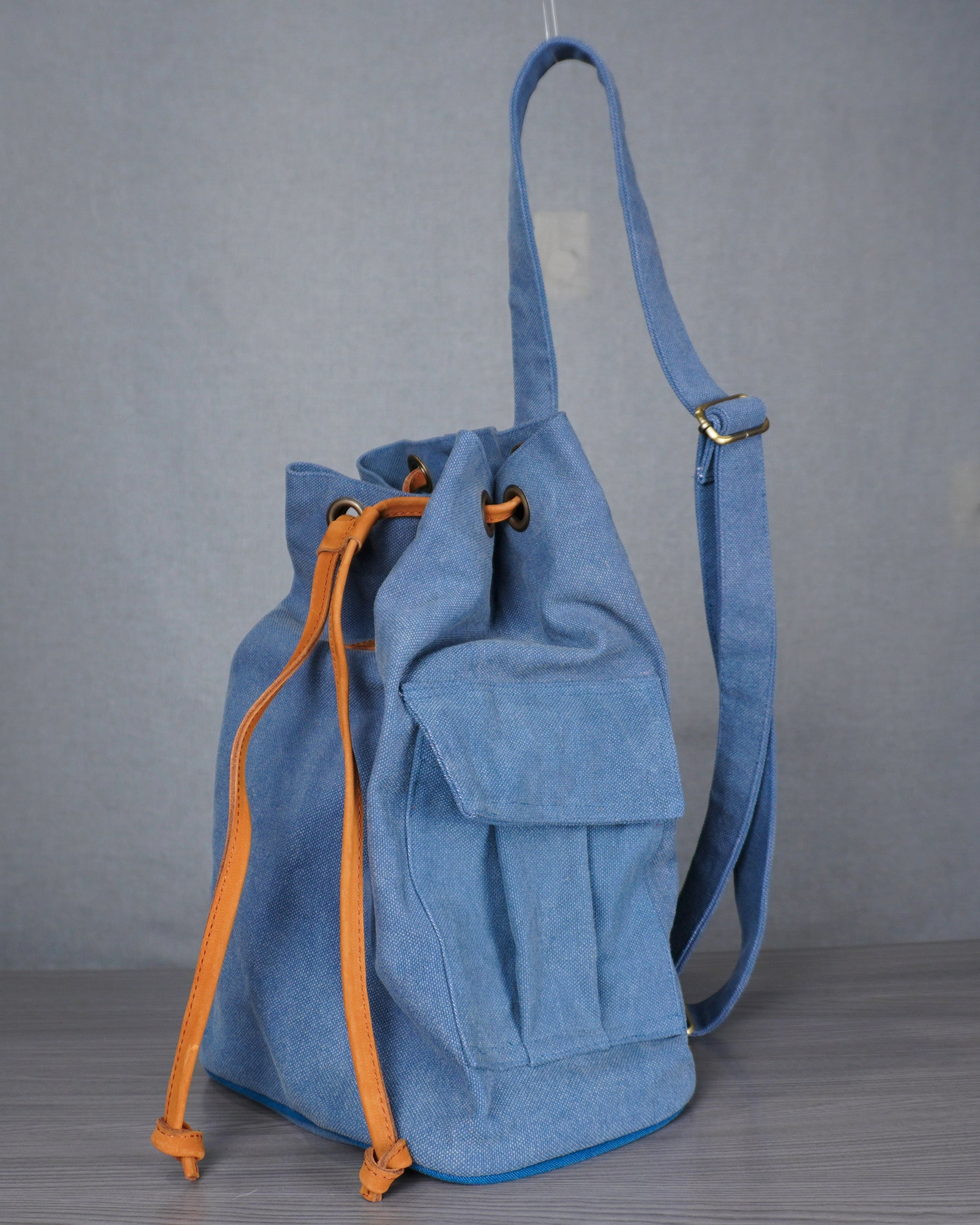 Blue backpack with orange drawstring on a gray floor against a plain wall.