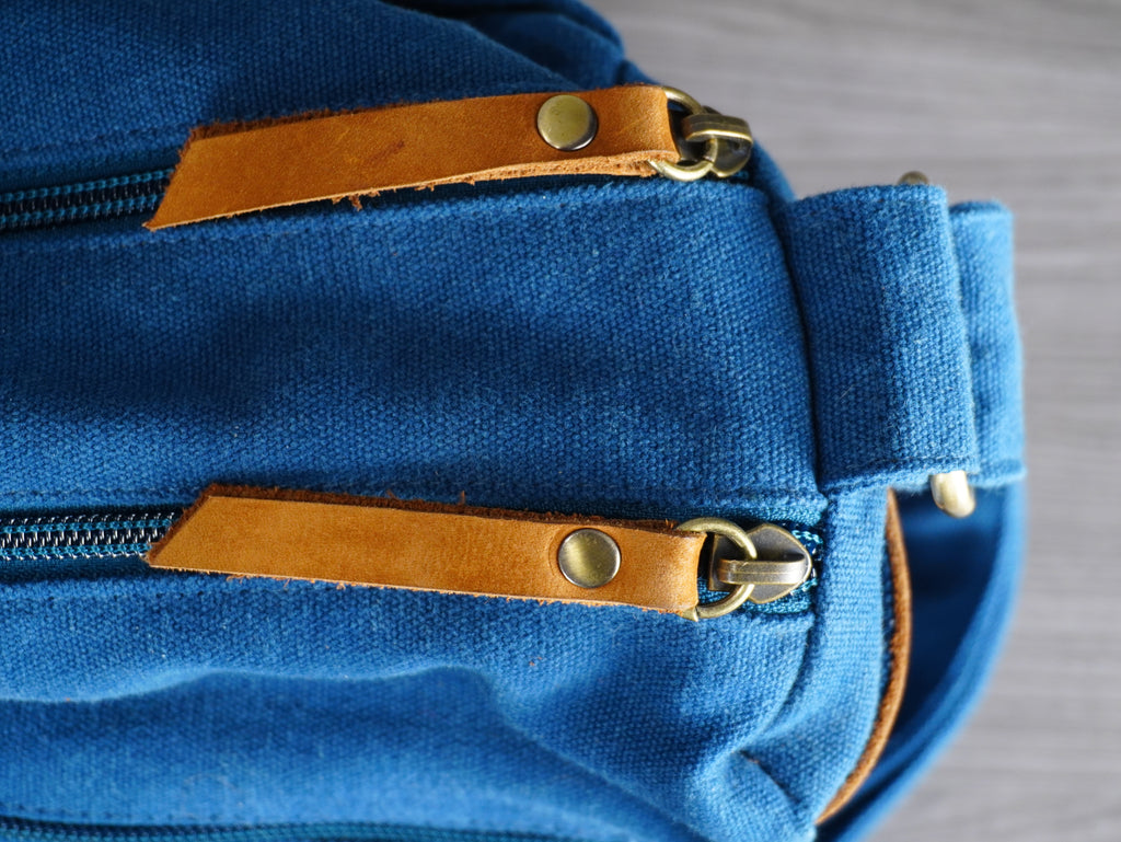 Blue bag with brown leather zippers on a gray background