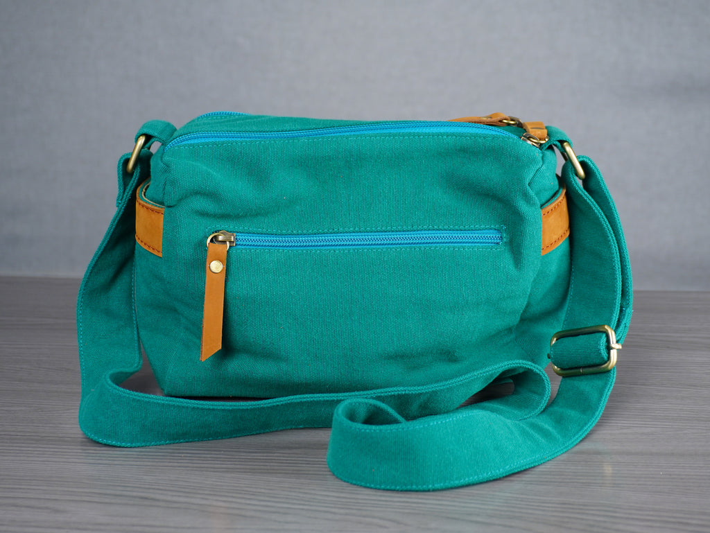 Teal handbag with leather accents on a gray surface and background