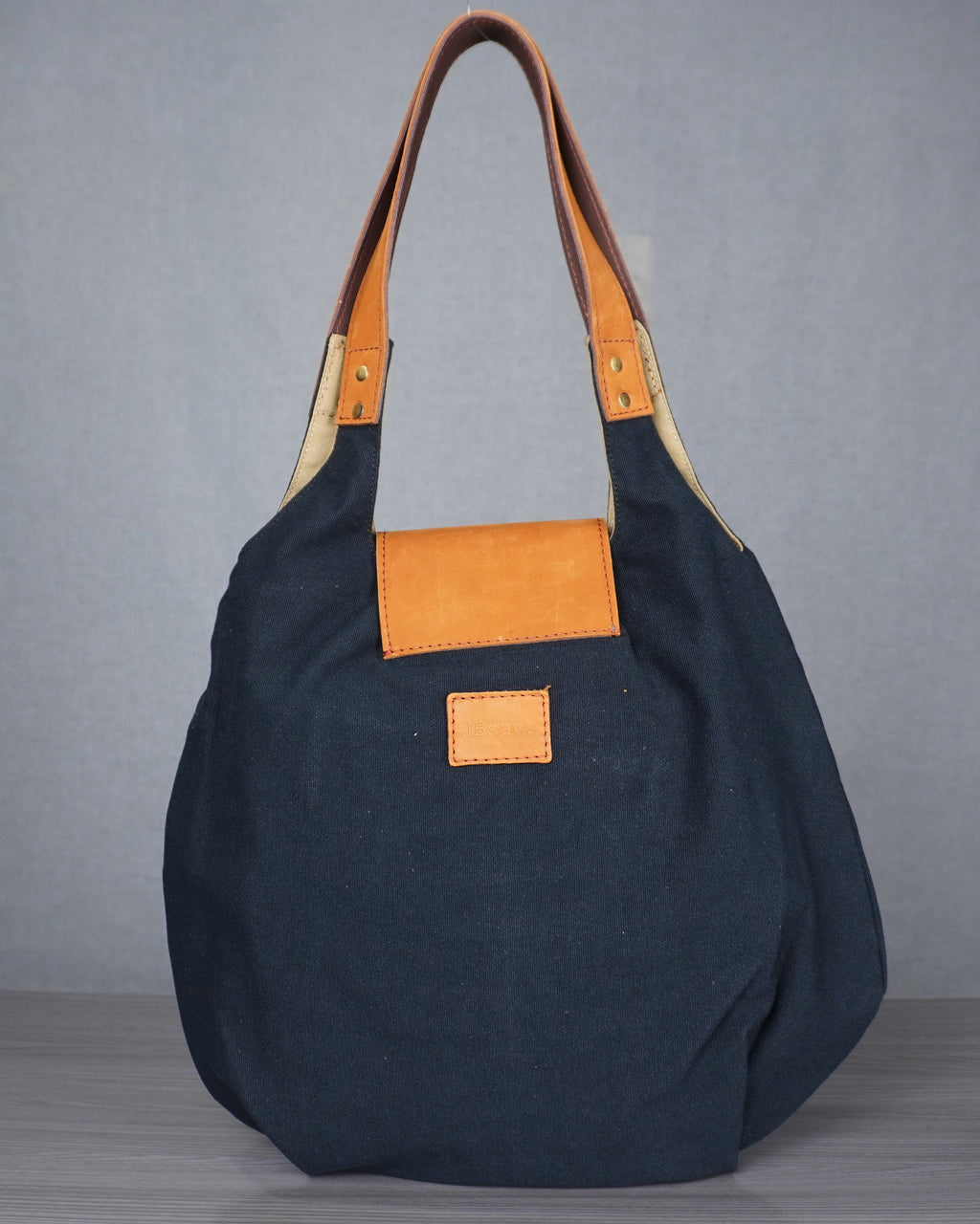 black handbag with leather accents on a gray surface against a blue and gray wall.