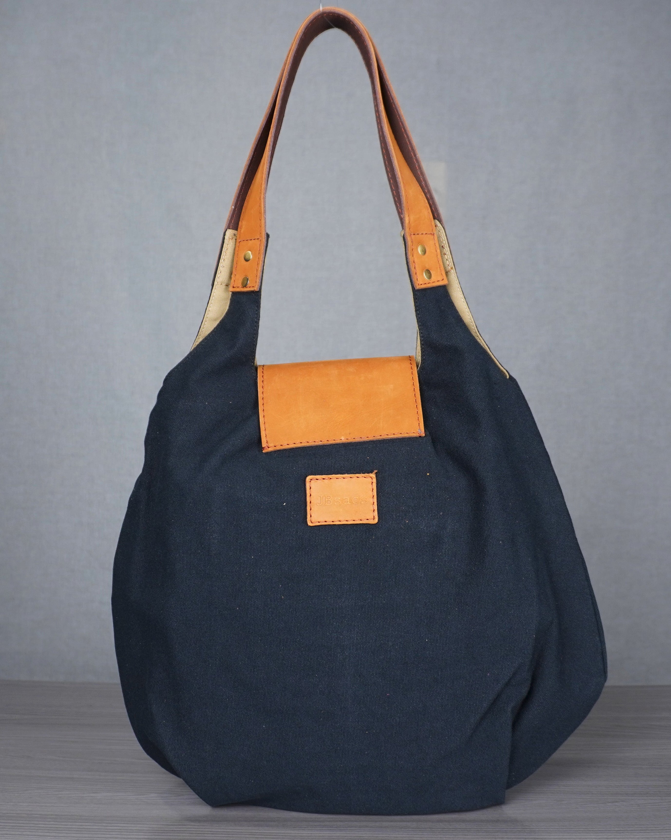 black handbag with leather accents on a gray surface against a blue and gray wall.