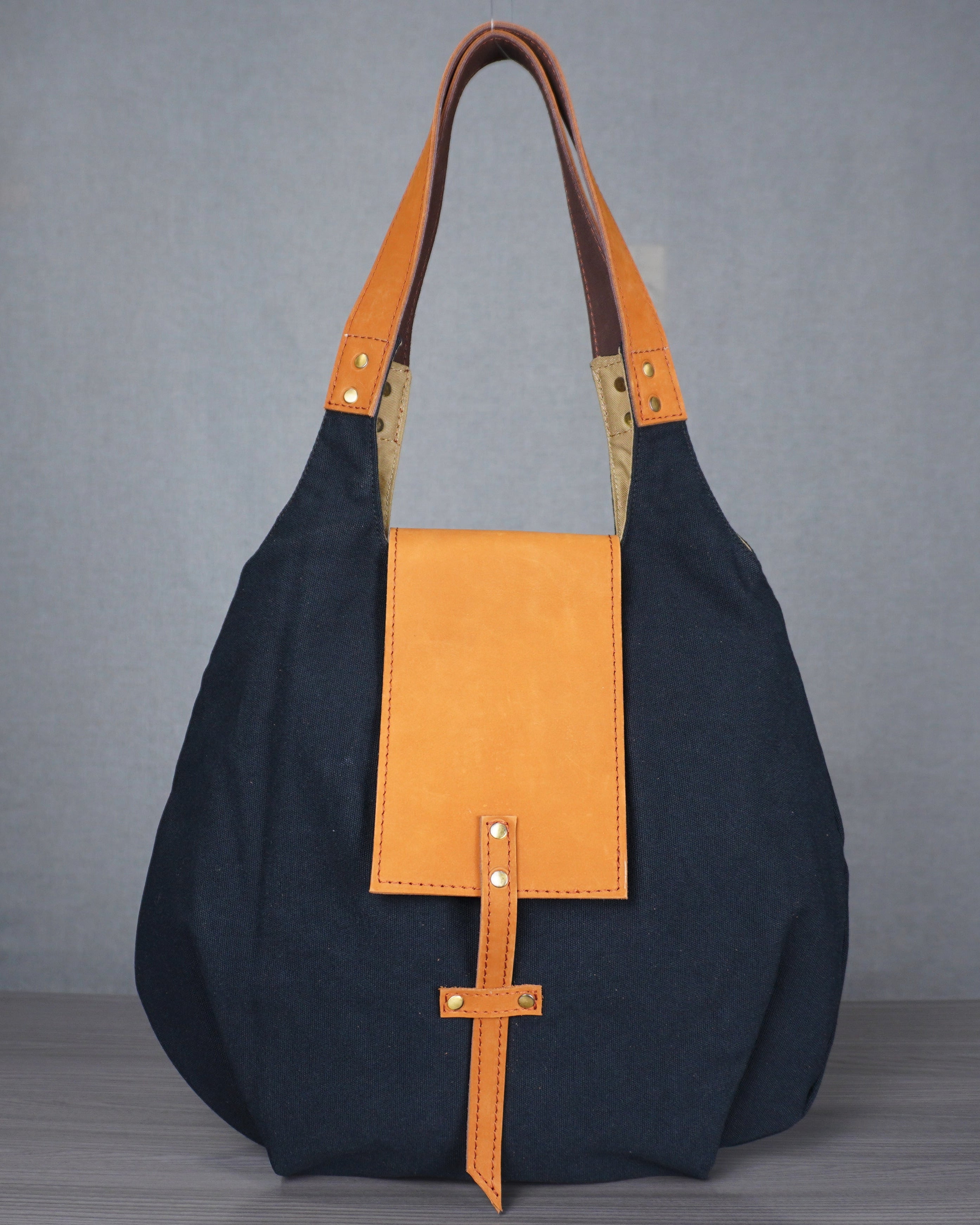 Black canvas and leather handbag on a gray surface with a blue wall background