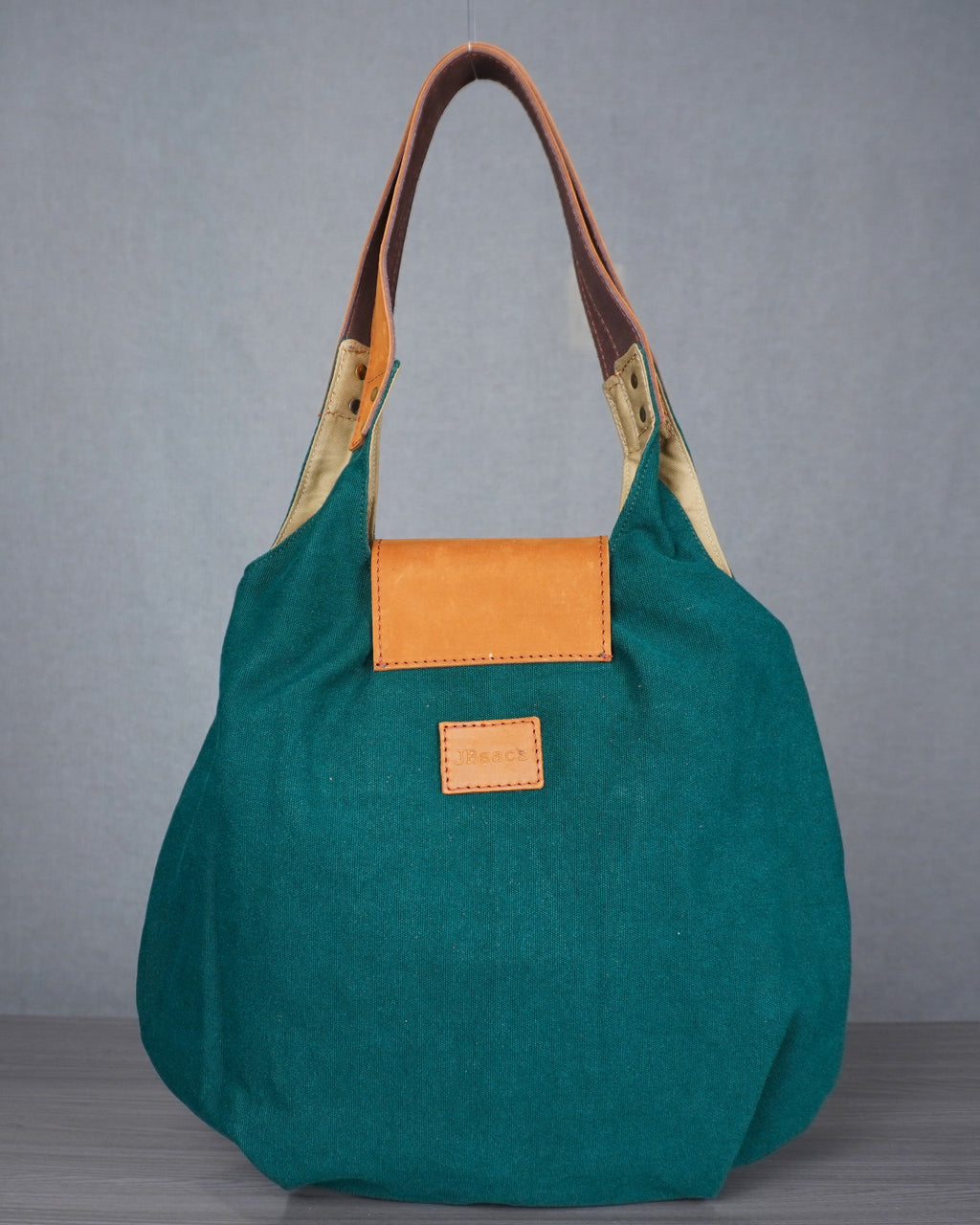 Green handbag with brown leather handle and orange patch on a gray background