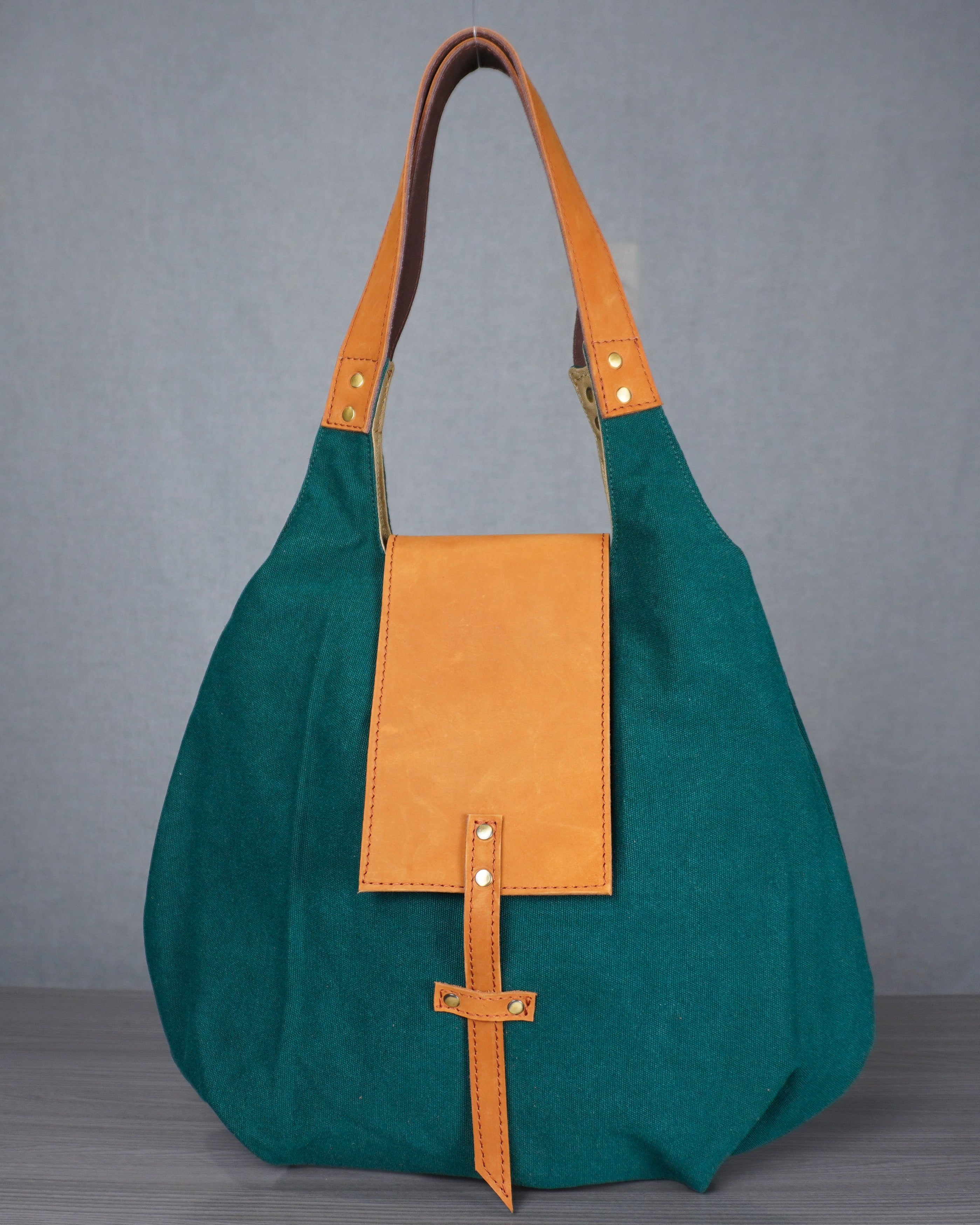 Green and orange handbag on a gray surface with a blue wall background
