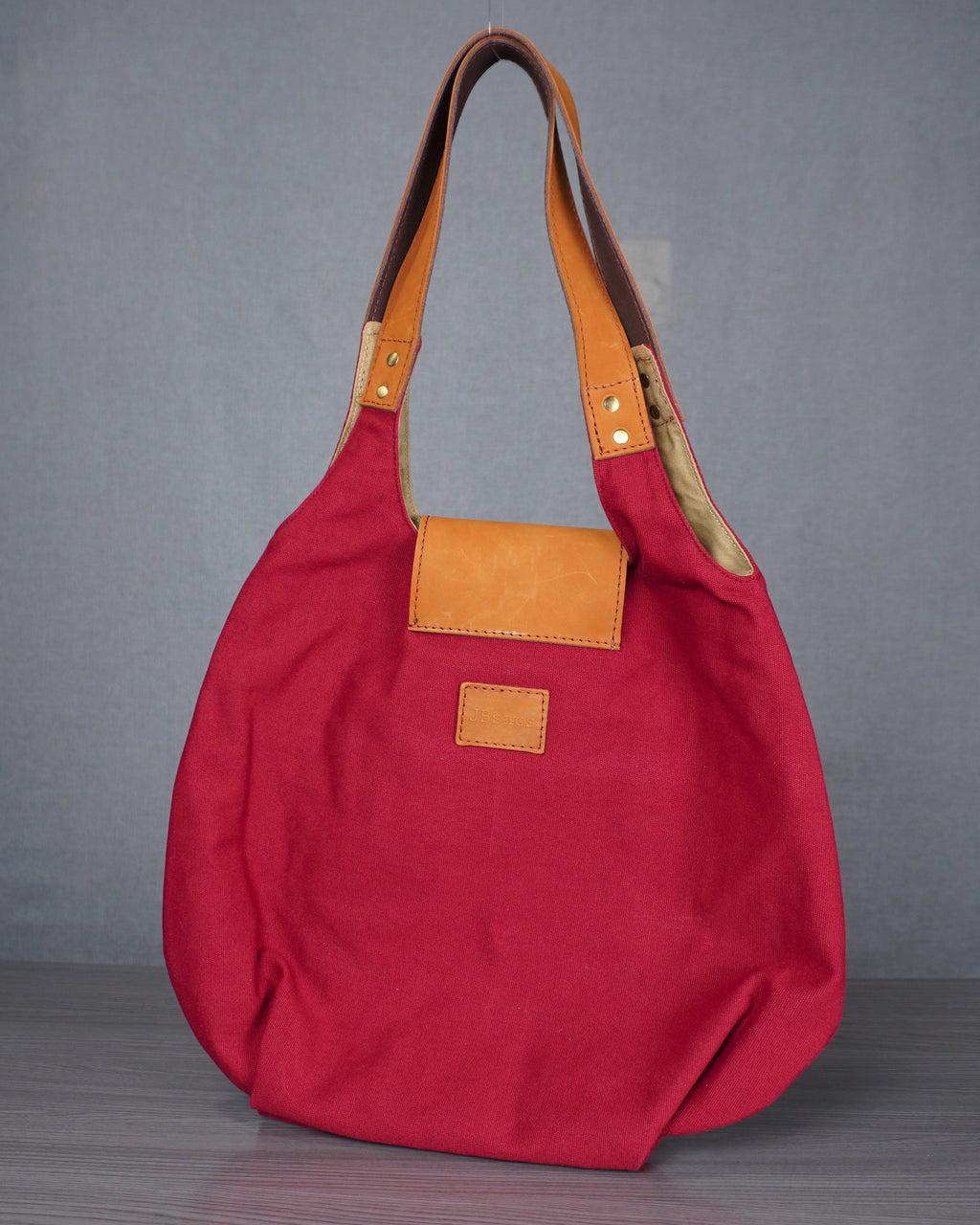 Red handbag with brown leather accents on a gray surface against a gray wall.