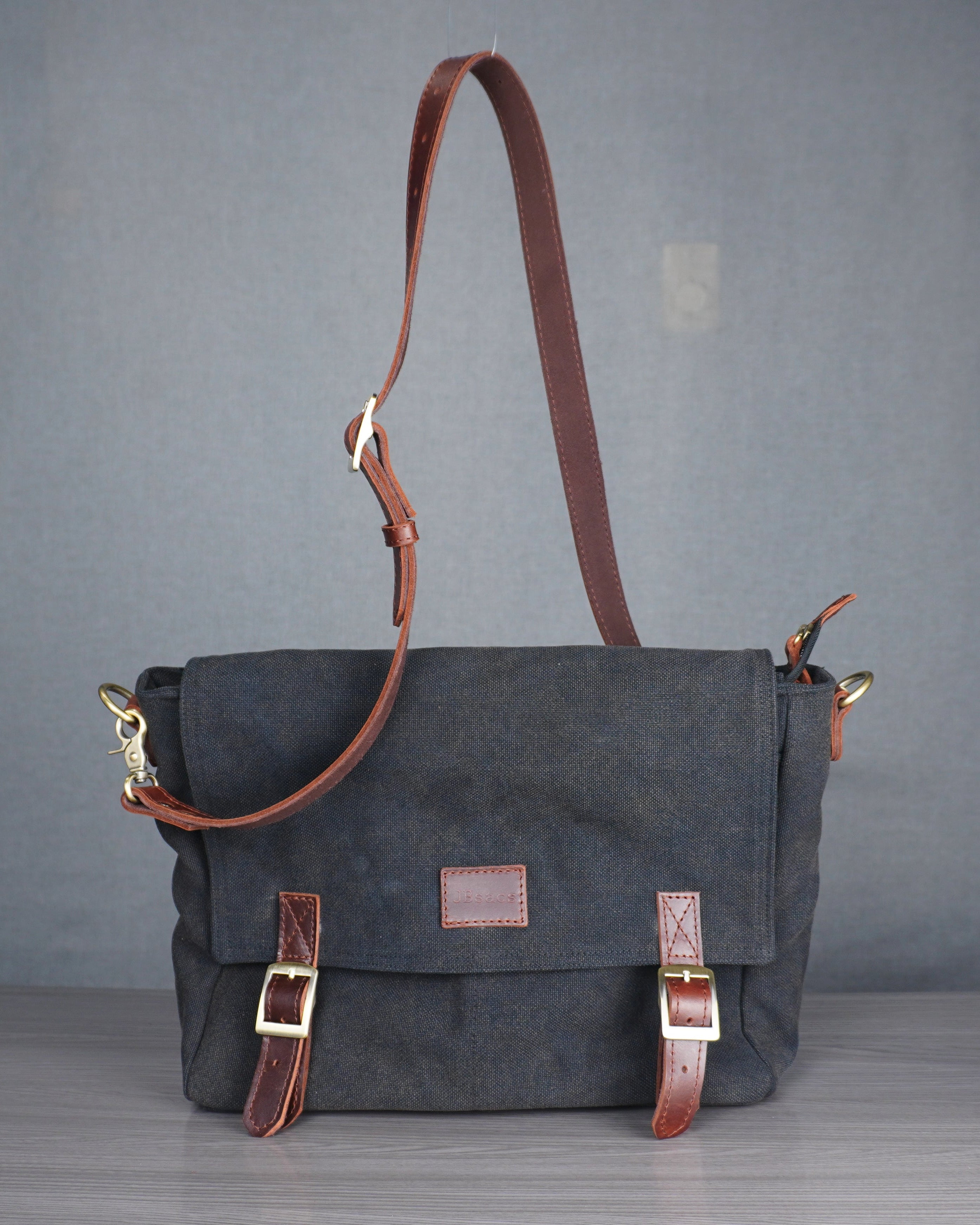 Gray bag with brown leather straps on a gray surface against a blue wall.