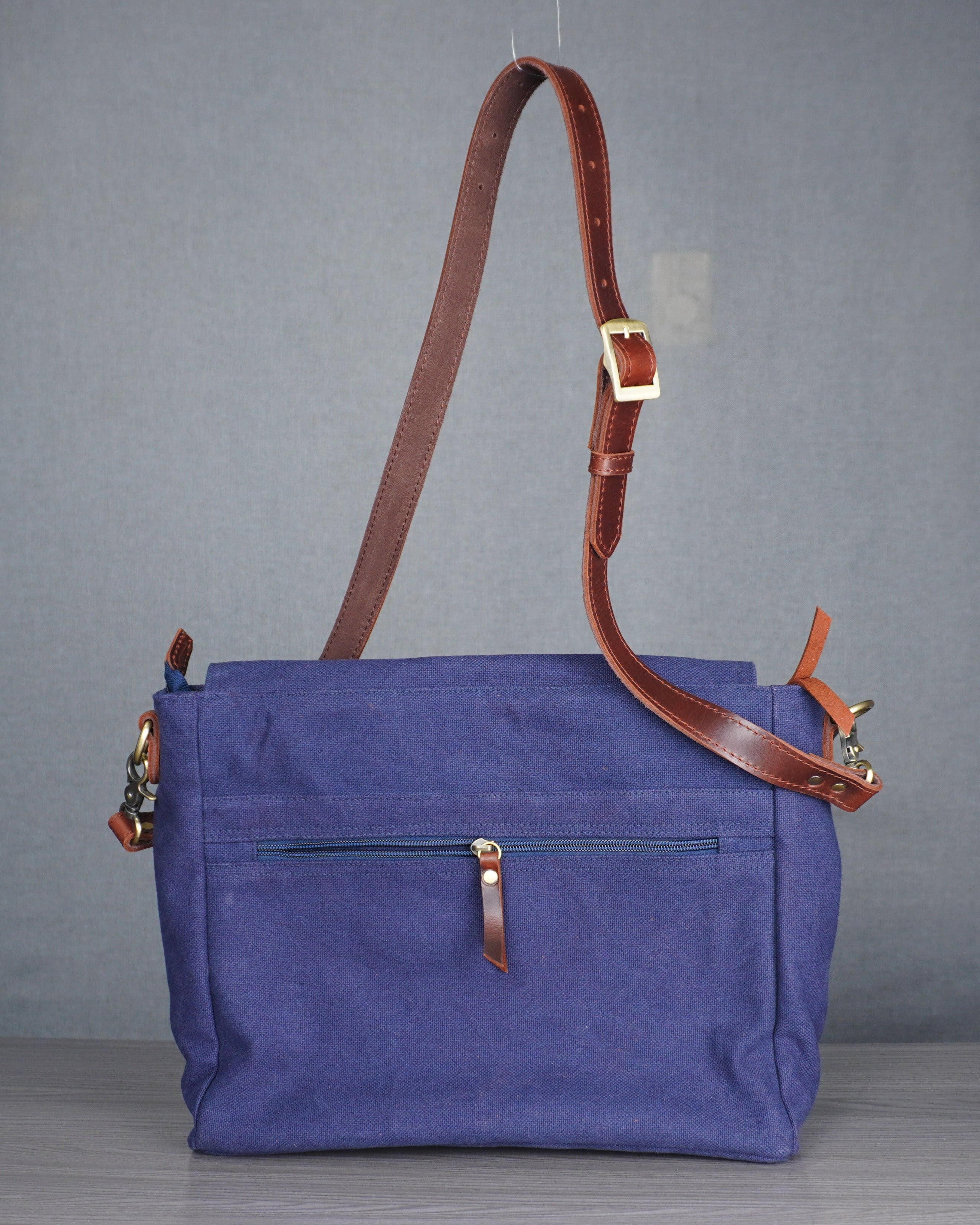 blue handbag with brown leather strap on a gray surface