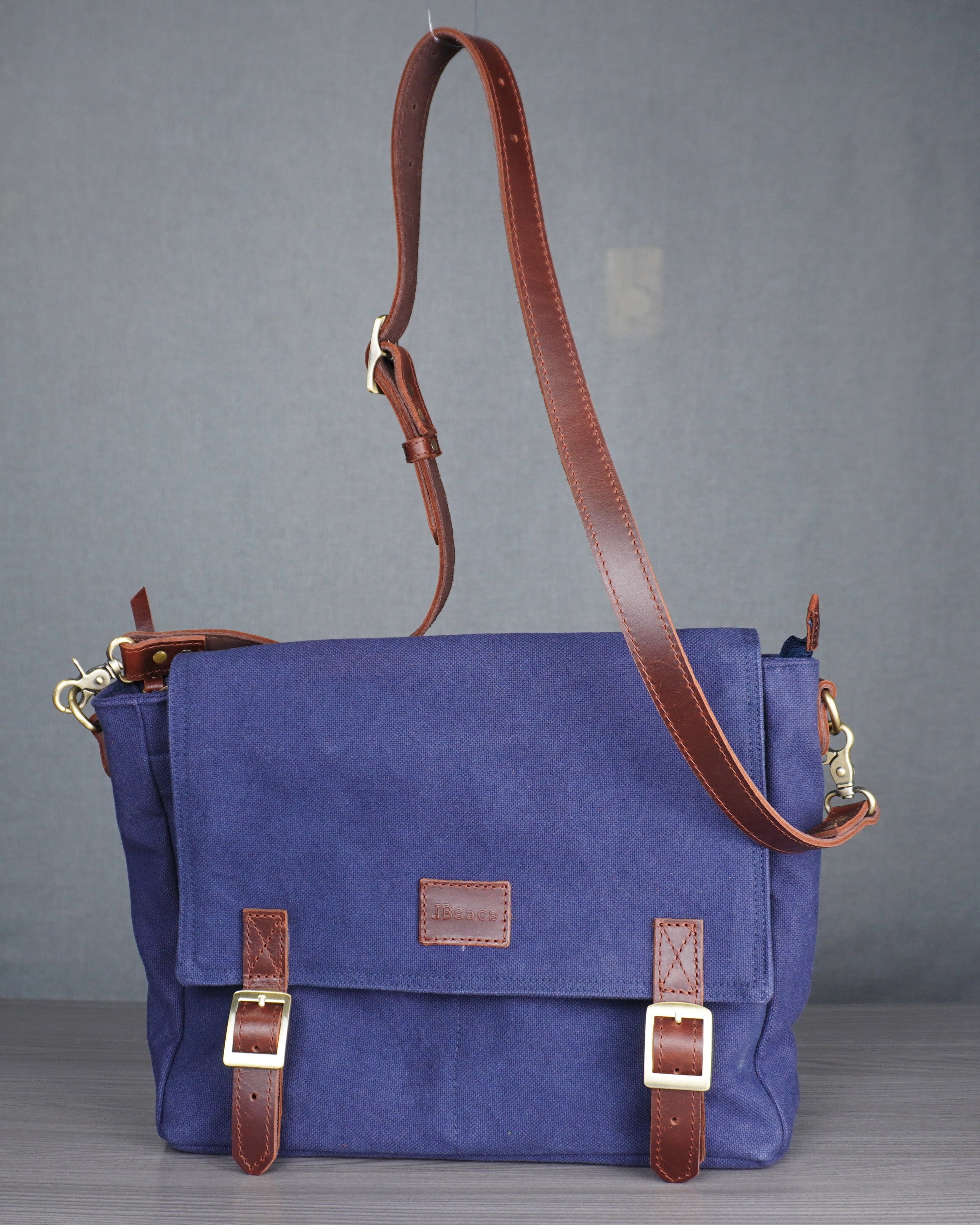 Blue bag with brown leather straps on a gray floor against a gray wall.