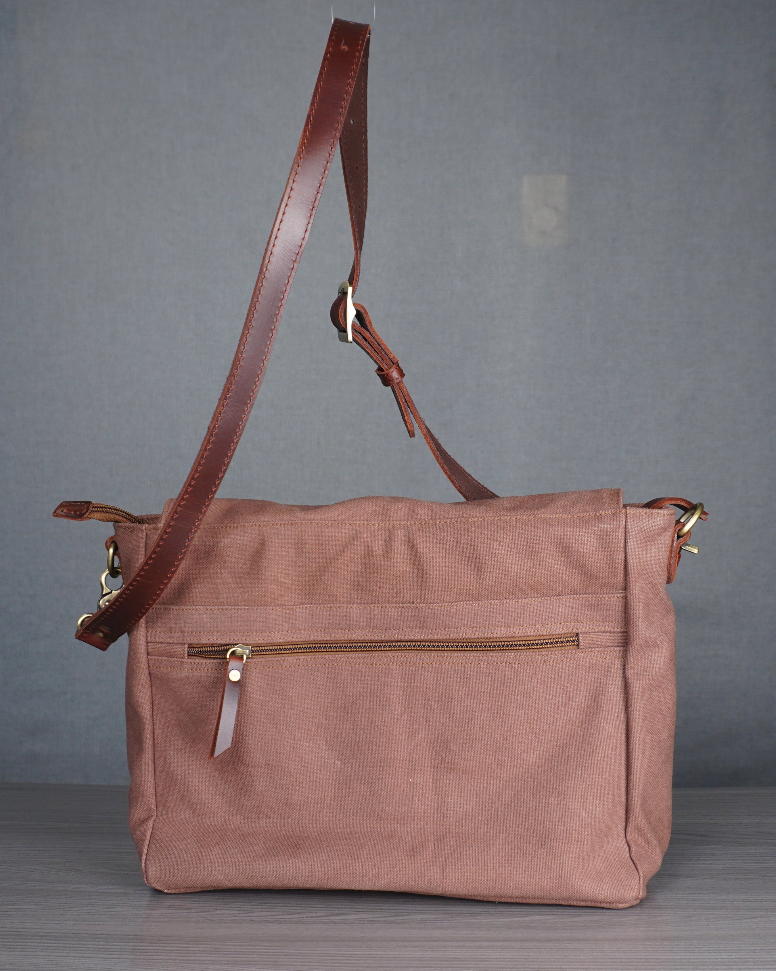 tan handbag with a brown leather strap on a gray surface against a gray wall.