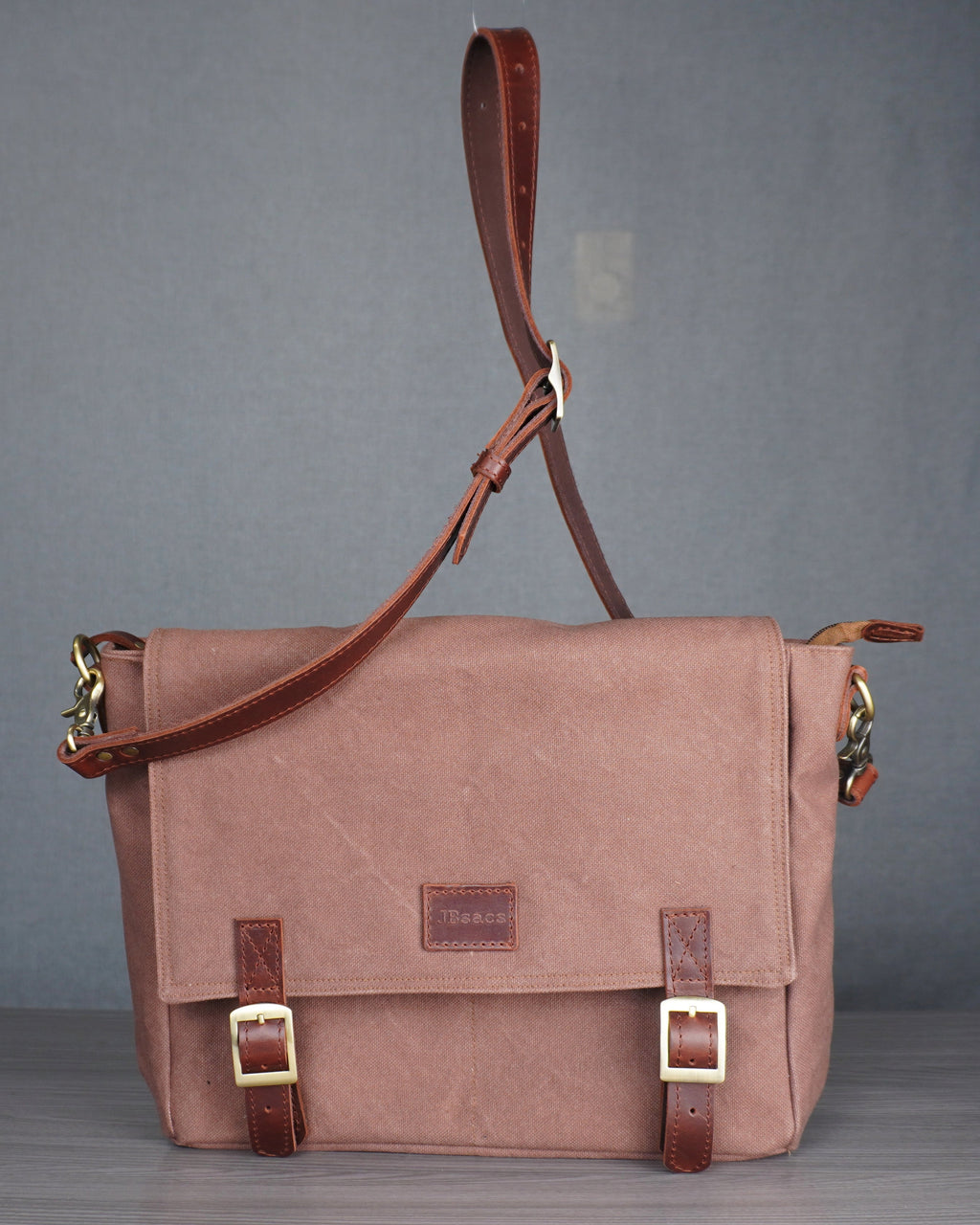 Brown leather satchel bag on a gray surface with a gray curtain background