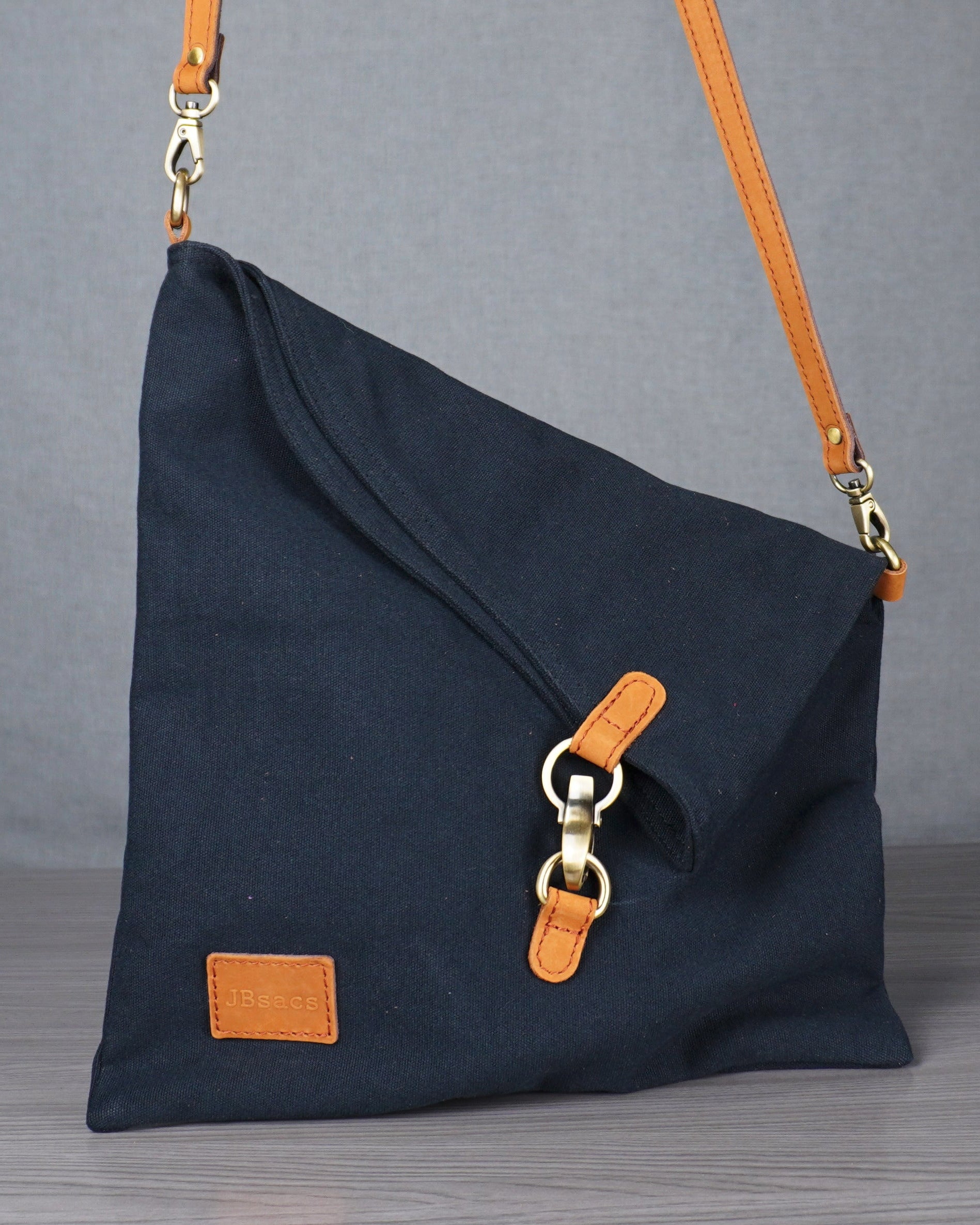 black handbag with orange accents on a gray surface against a gray curtain background