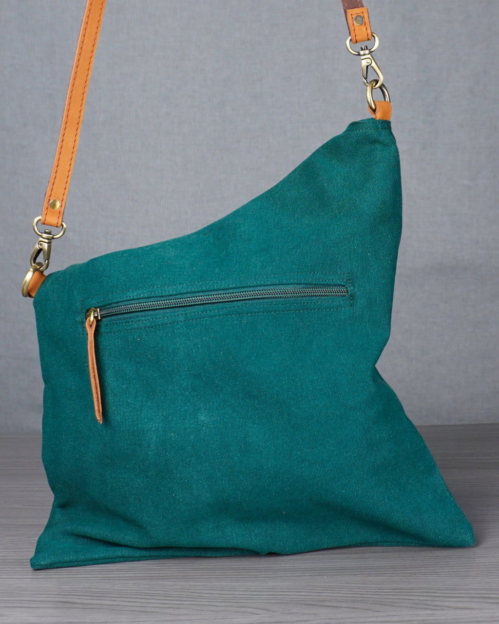 Teal handbag with a strap on a gray surface against a plain background