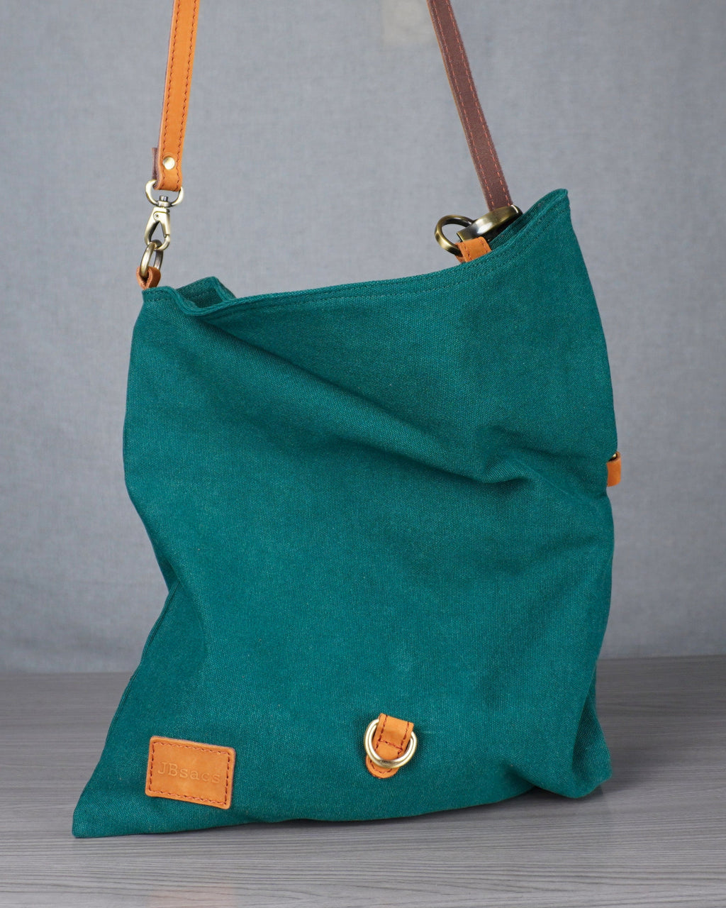 Teal handbag with orange accents on a gray surface against a gray wall.
