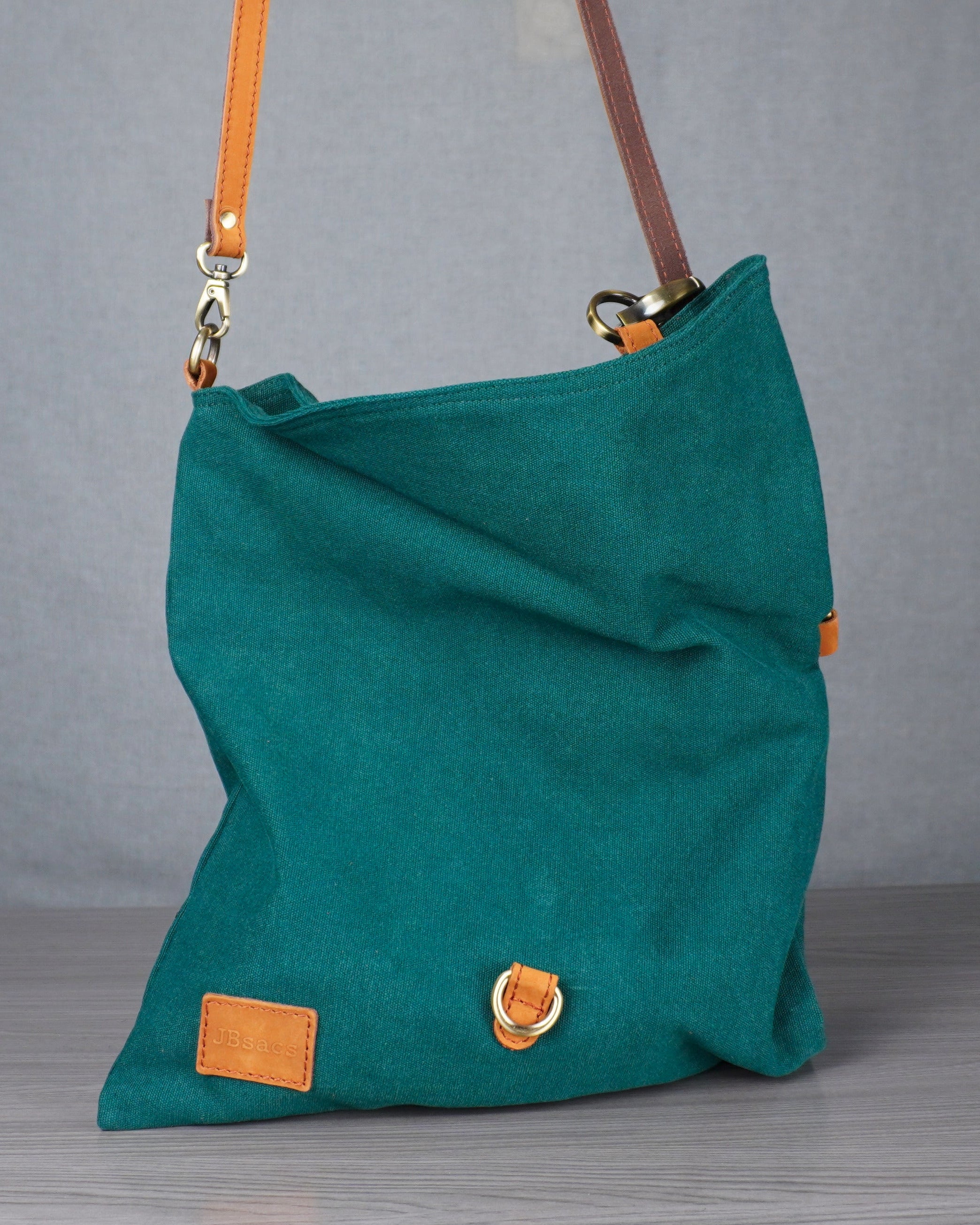 Teal handbag with orange accents on a gray surface against a gray wall.