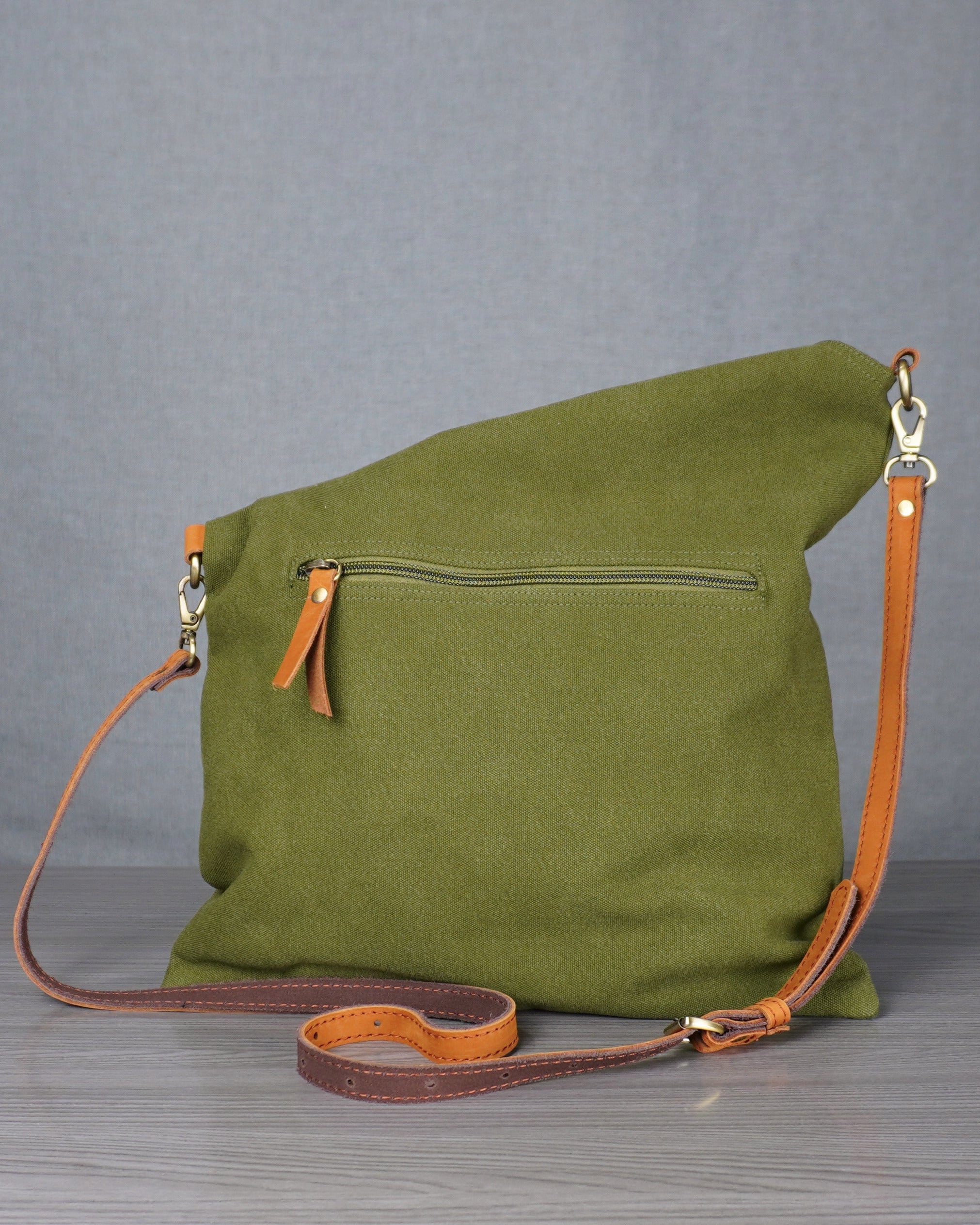 Green bag with brown strap on a metal surface against a gray curtain background
