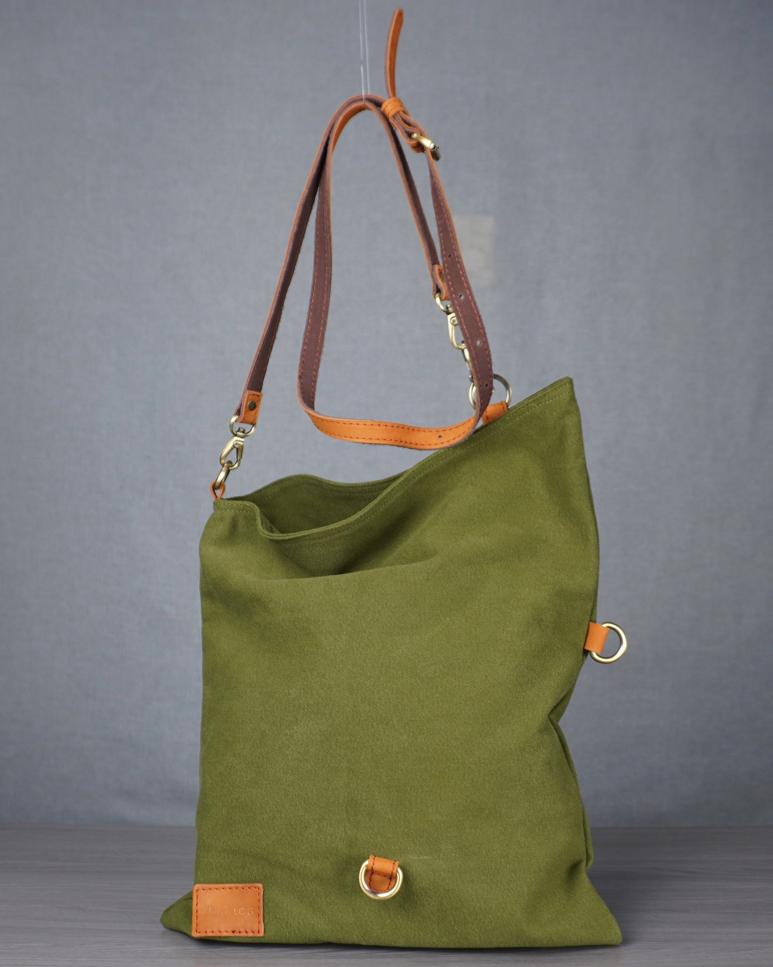 green bag with tan leather handle on a grey table
